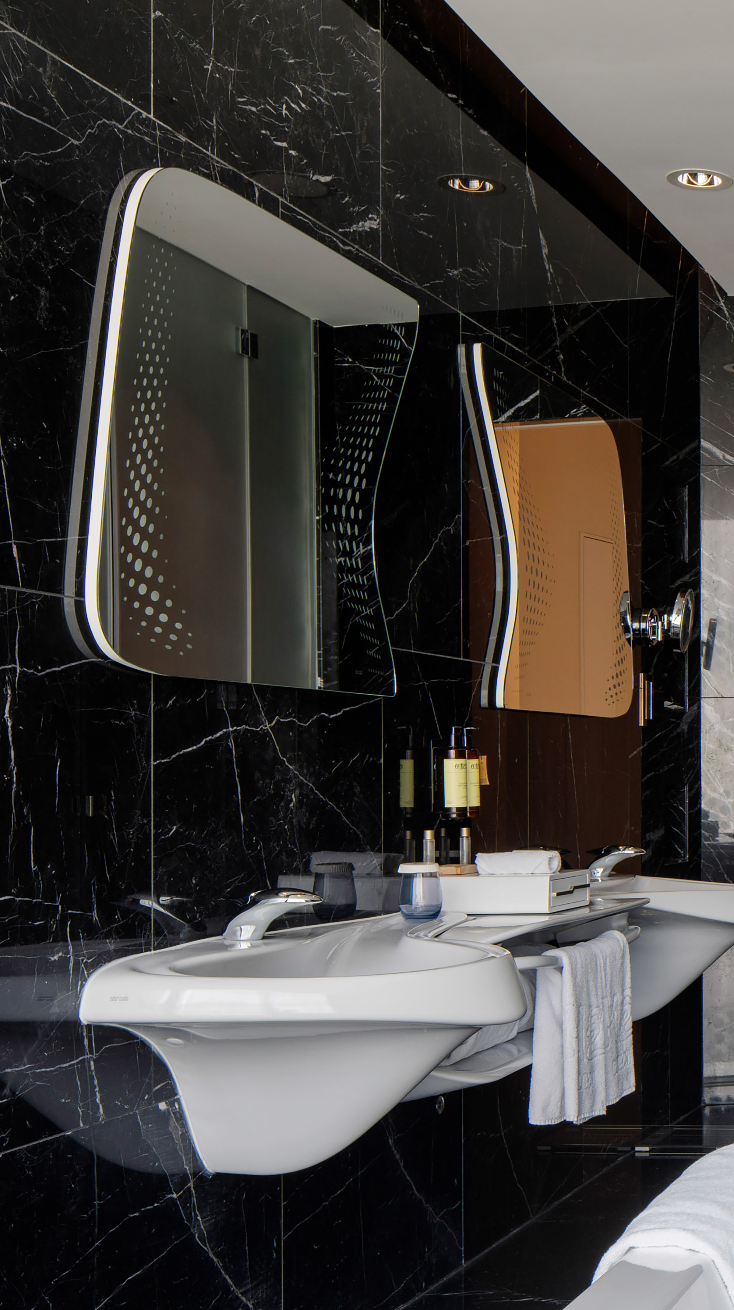 Modern black marble bathroom with sleek white sink and illuminated designer mirrors.