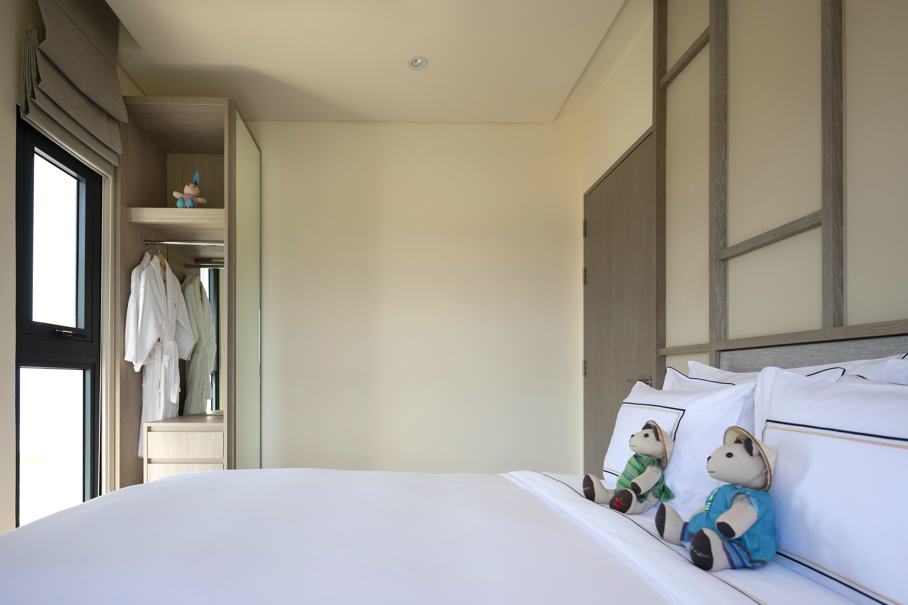 Modern hotel bedroom with white bed, two teddy bears, and open closet.