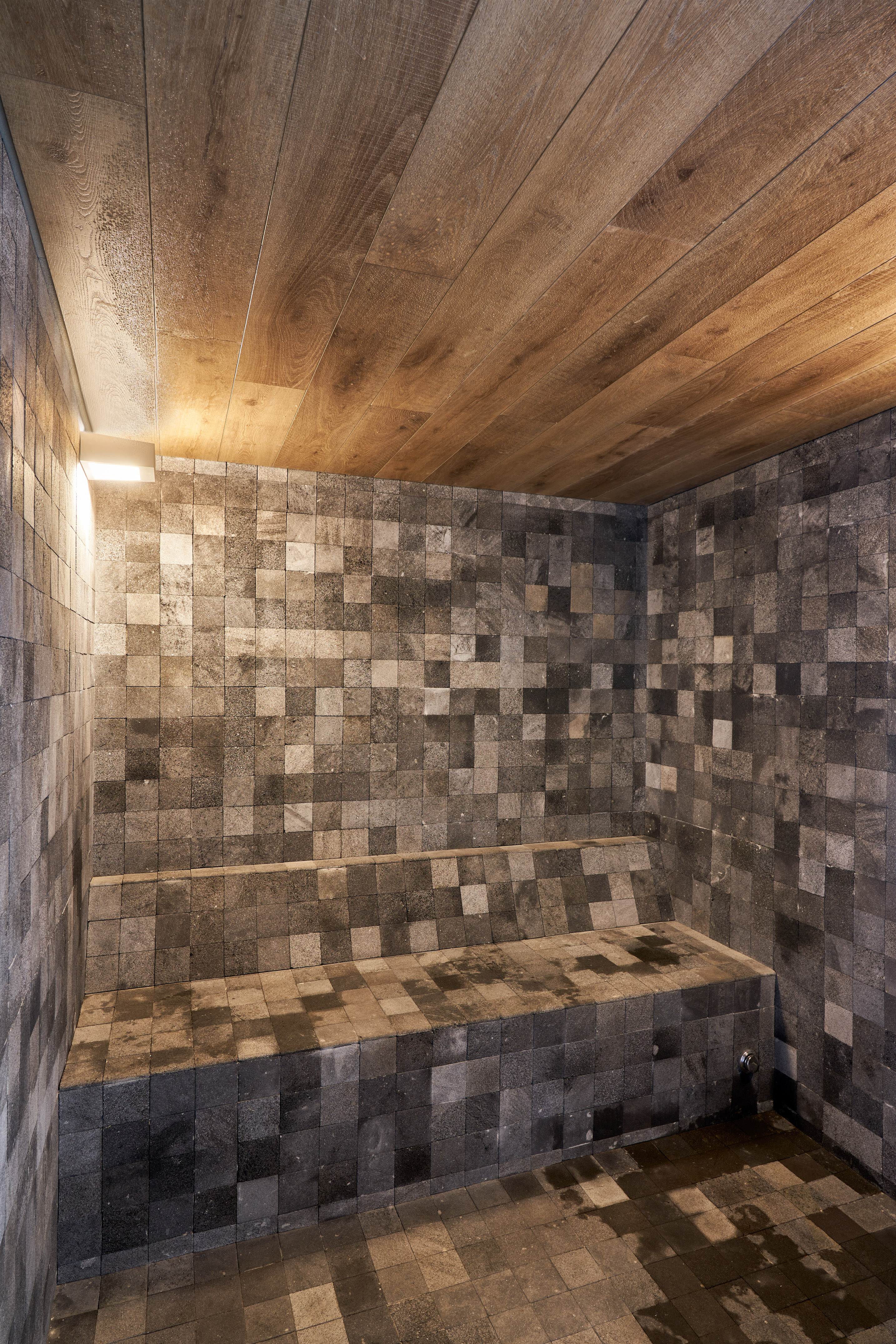 Modern steam room with dark stone tiles, built-in bench, and wooden ceiling.