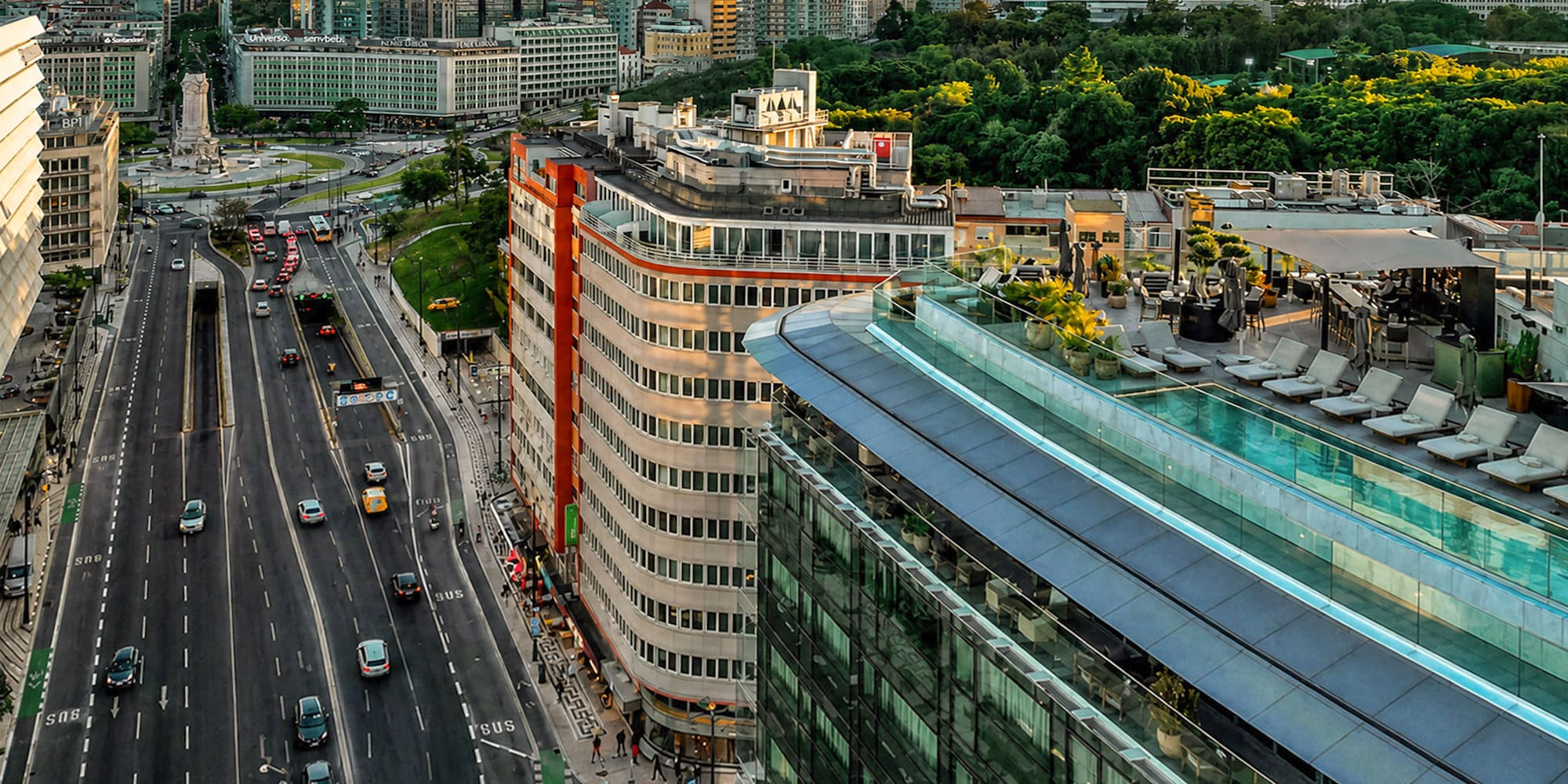 Aerial view of Lisbon city with busy highway, modern buildings, and rooftop pool.
