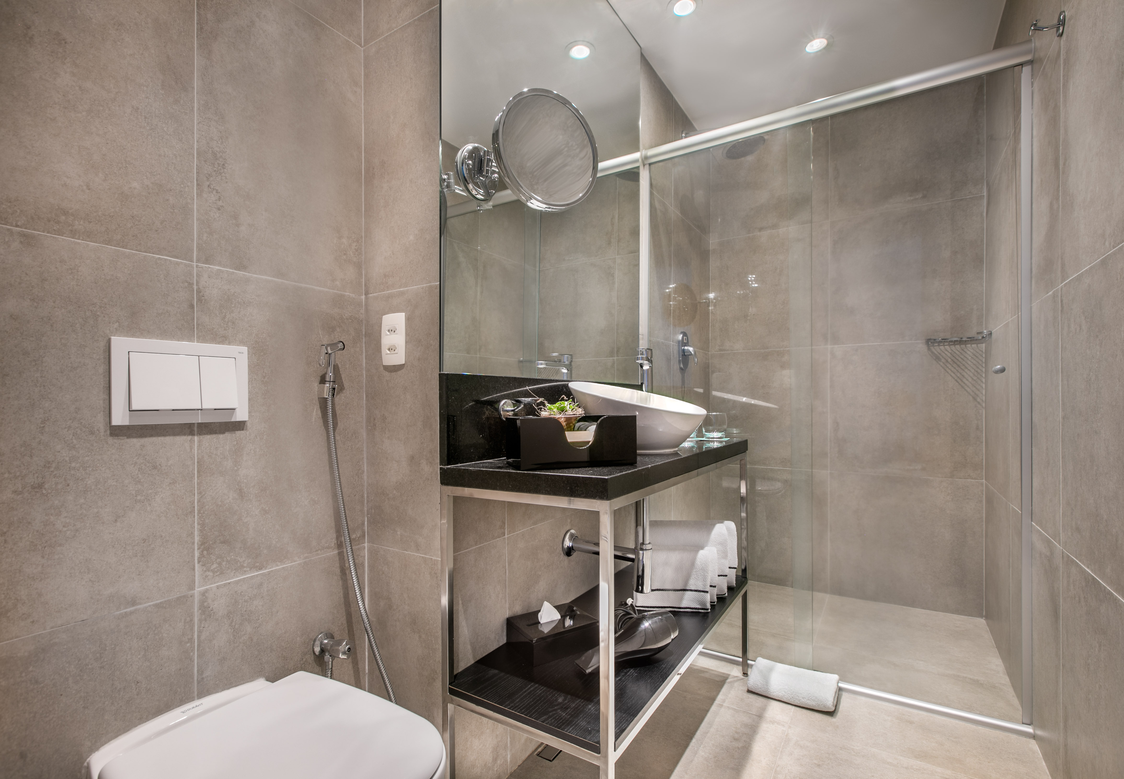 Modern bathroom with beige tiled walls, white toilet, vanity sink, and glass shower.