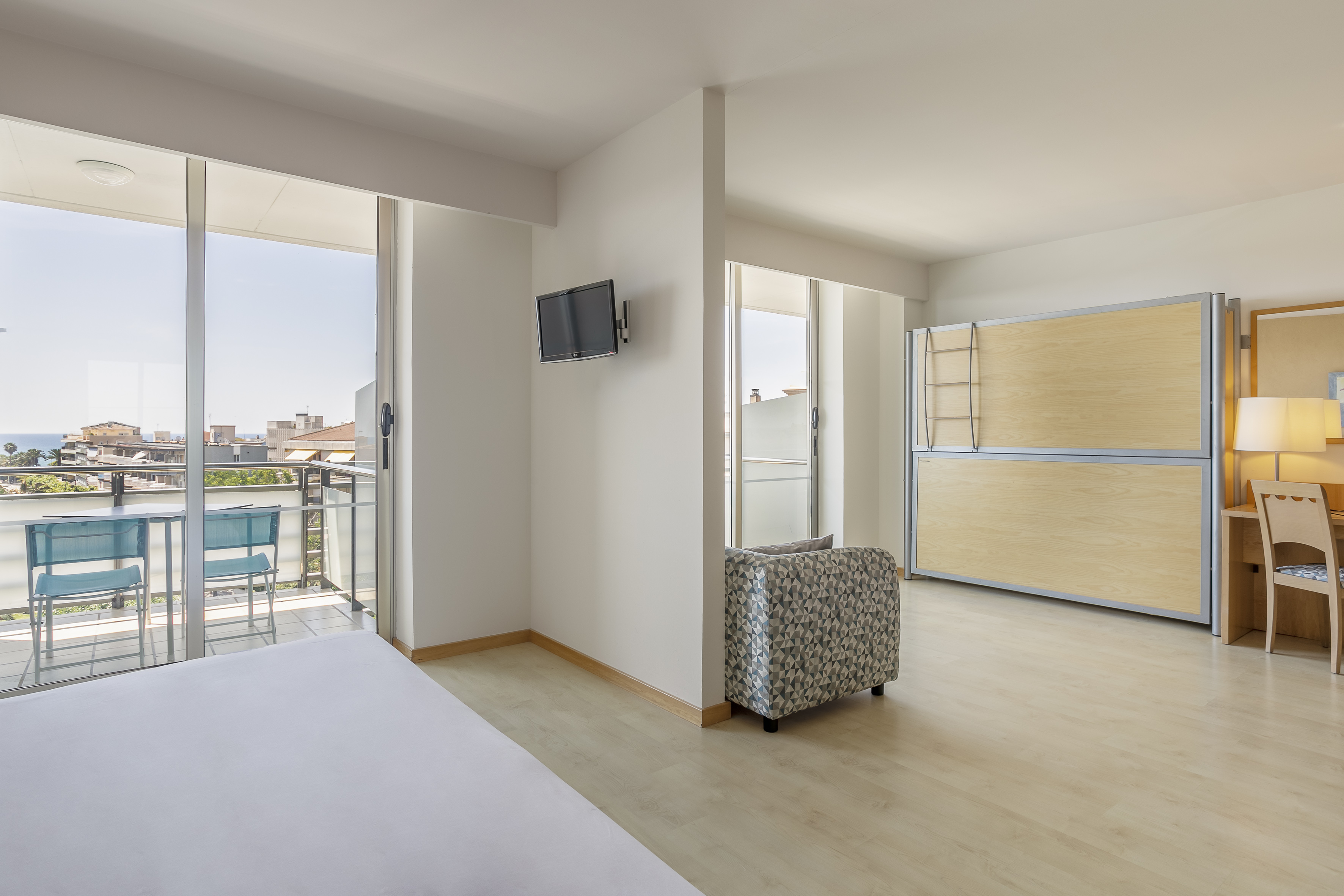 Bright hotel room with sea view balcony, bed, wall TV, and built-in bunk beds.