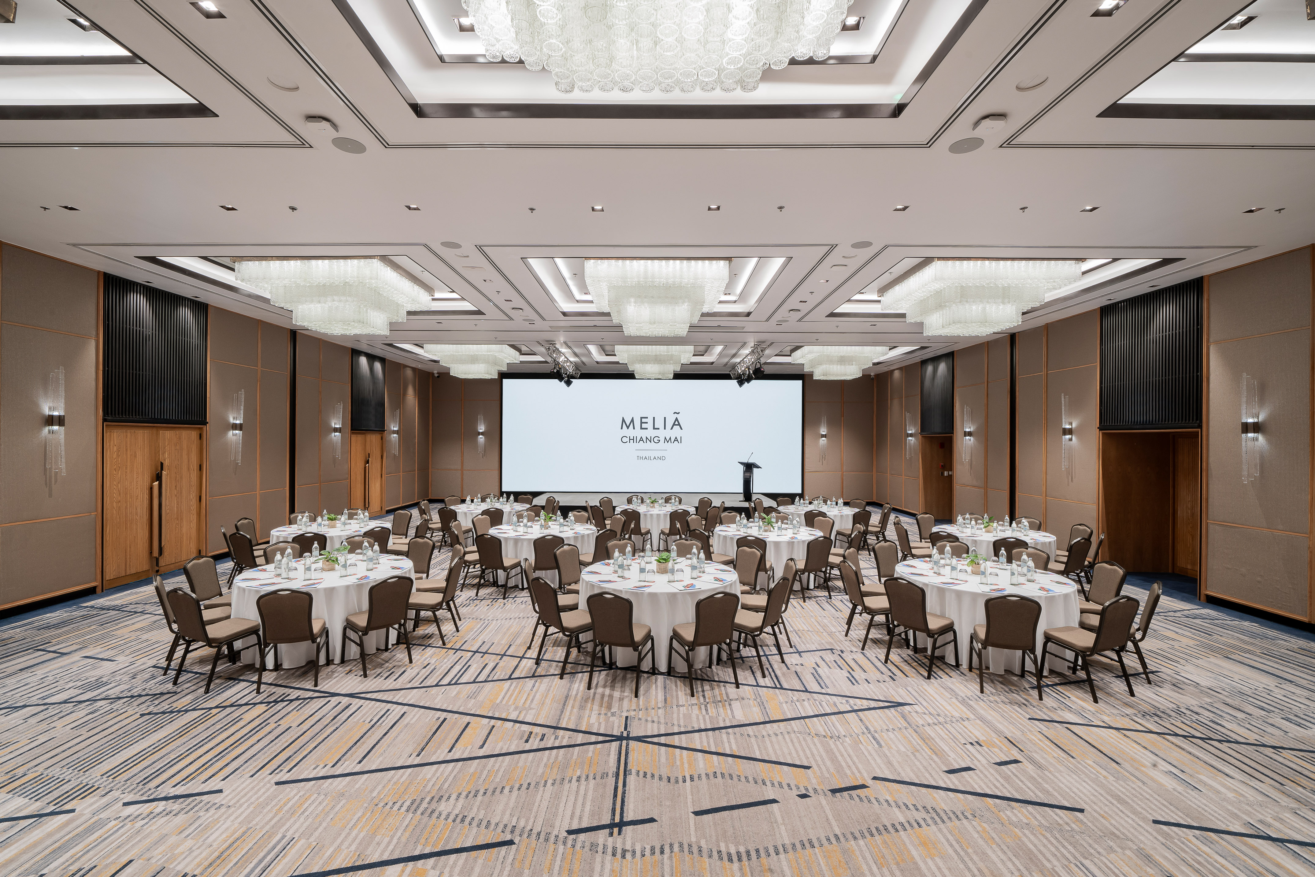 Elegant Meliá Chiang Mai event ballroom with round tables and large screen.