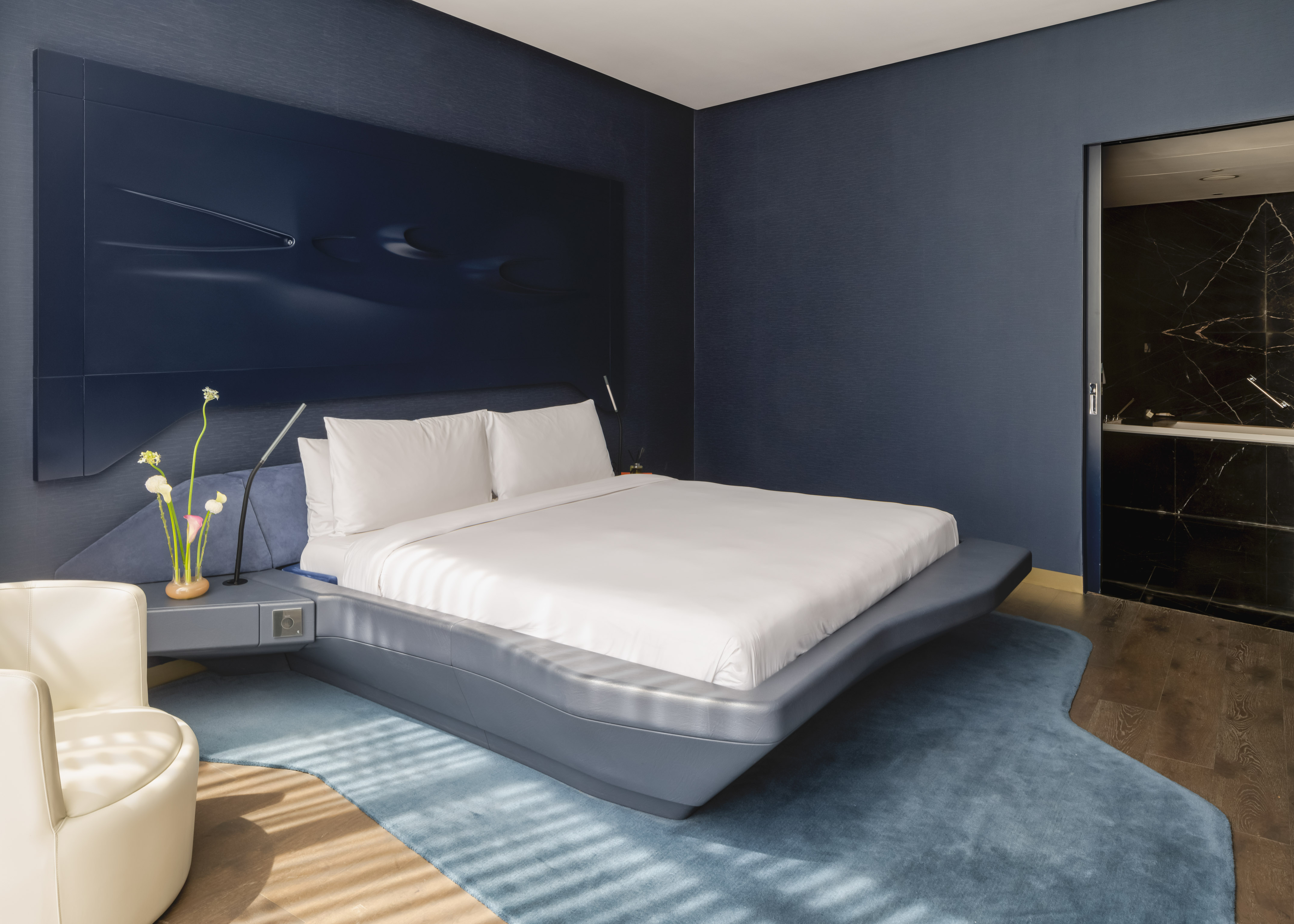 Sleek deep blue modern bedroom with large bed and unique sculpted headboard.