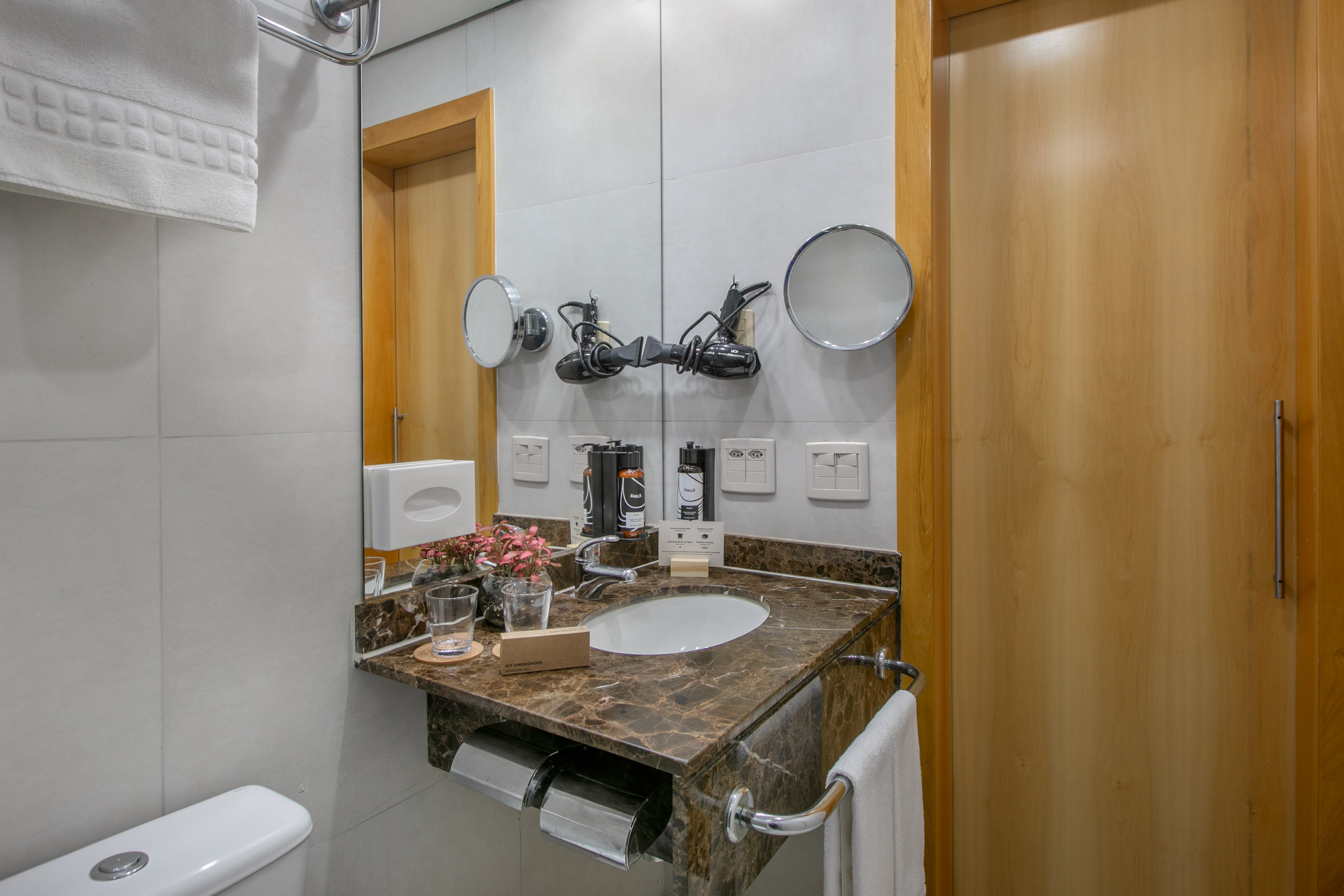 Hotel bathroom vanity with marble sink, amenities, hair dryer, and mirrors.