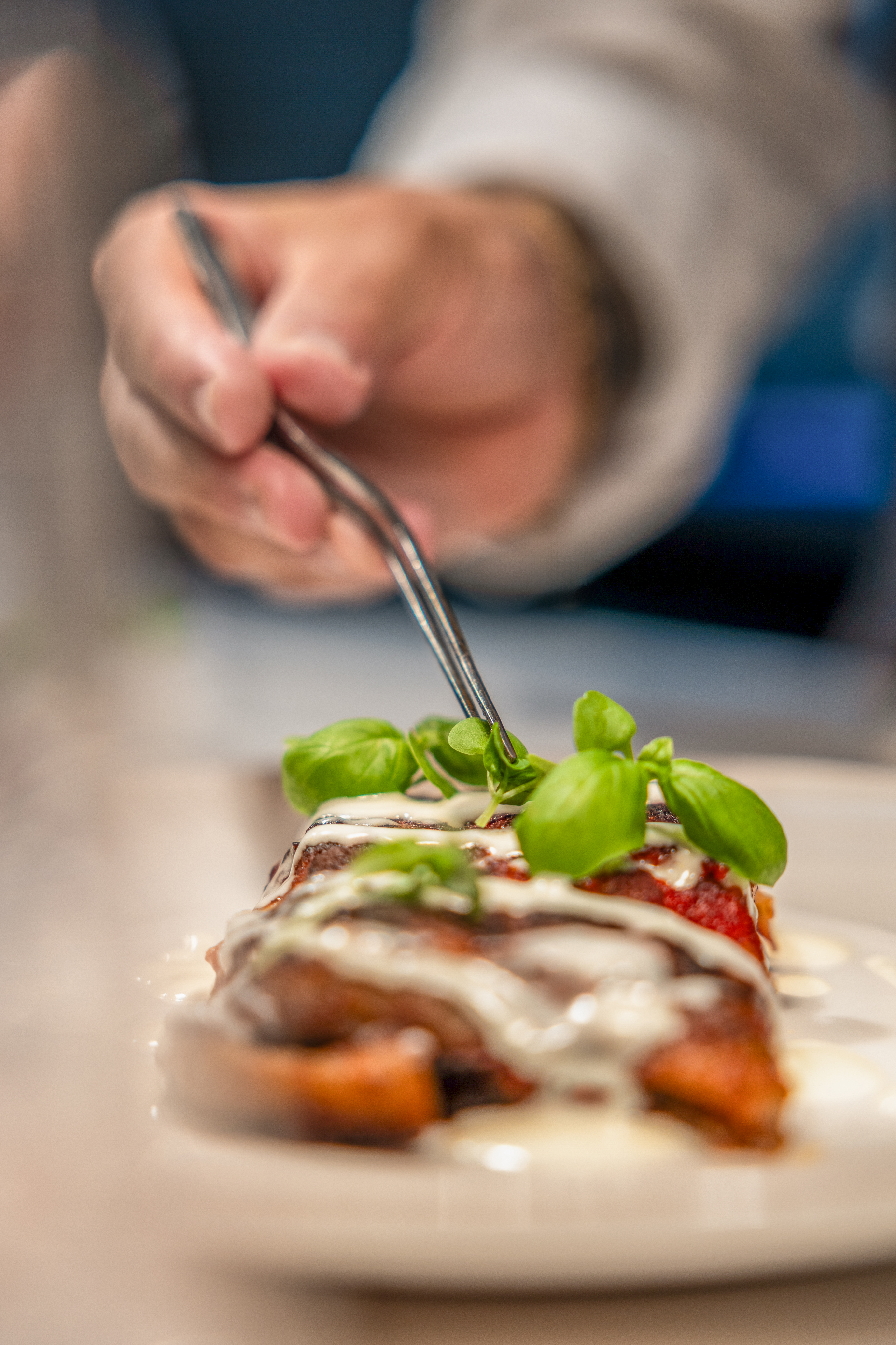 Chef's hand garnishing a gourmet dish with fresh basil using tweezers.