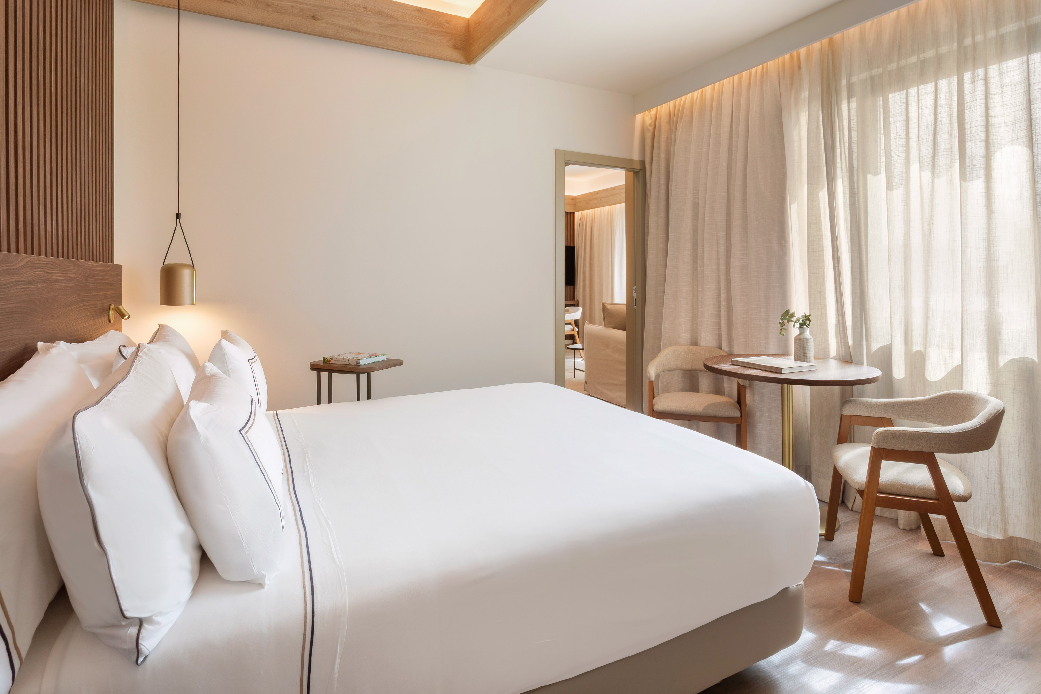 Modern hotel bedroom with white bed, wooden accents, and natural light.