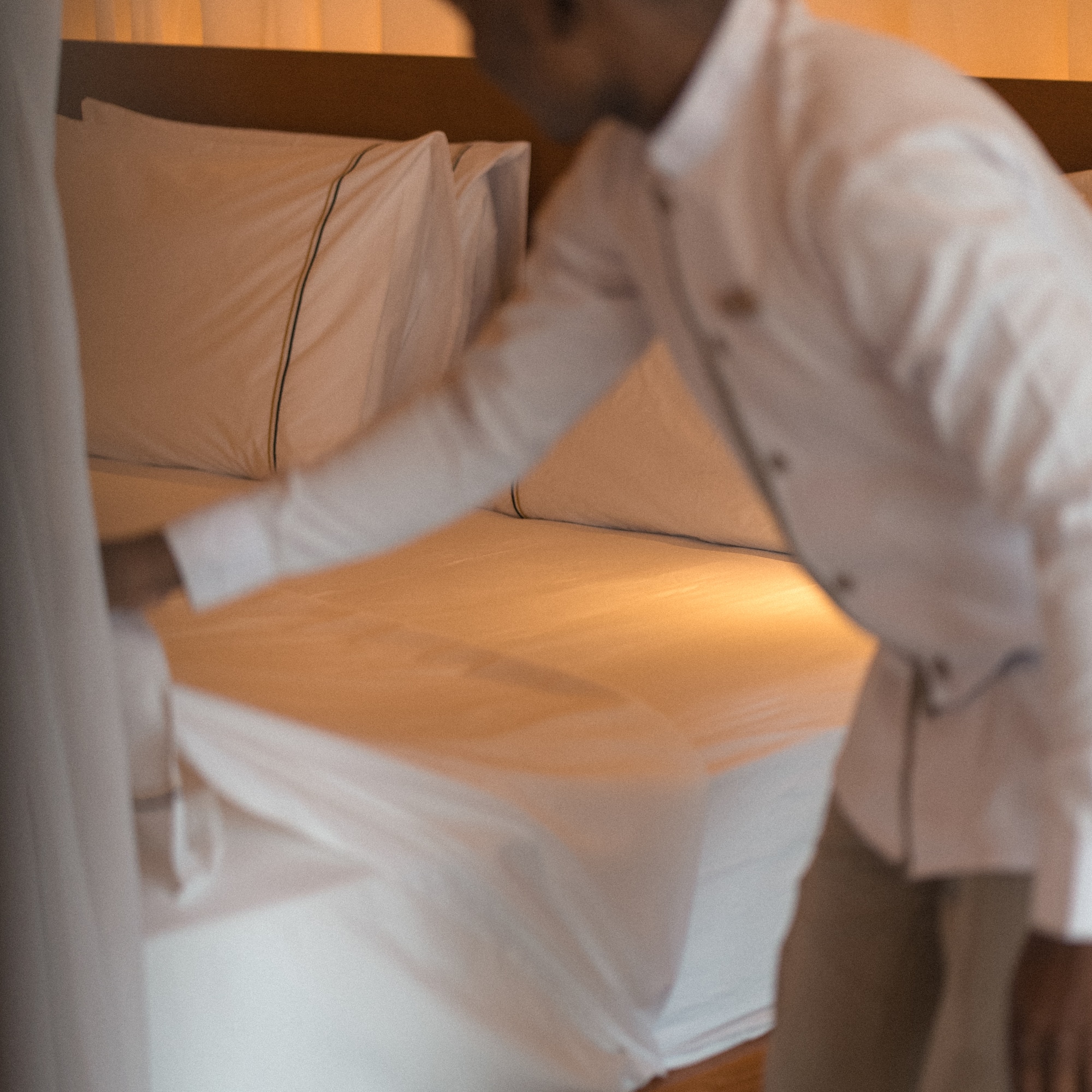 Housekeeping staff neatly making a bed with fresh white sheets.