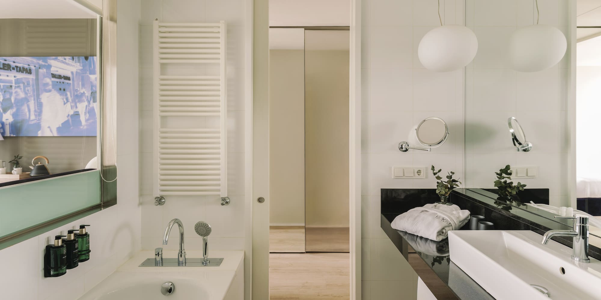 Modern hotel bathroom with white bathtub, sink, black counter, and wood floor.
