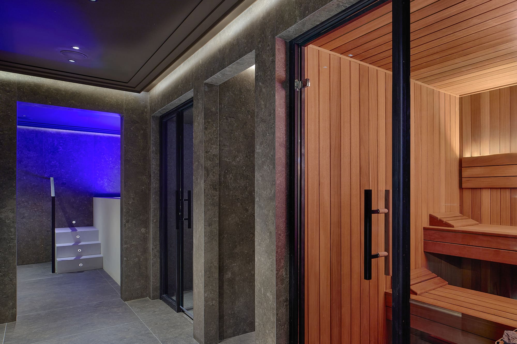 Luxury spa interior with open sauna, steam room, and blue-lit plunge pool.