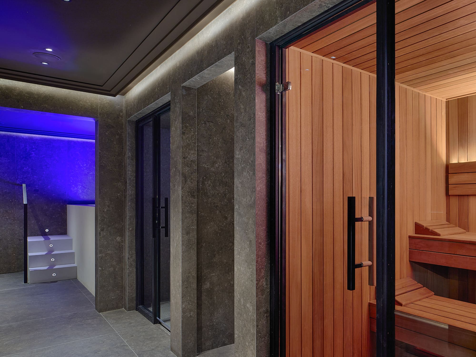 Luxury spa interior with open sauna, steam room, and blue-lit plunge pool.