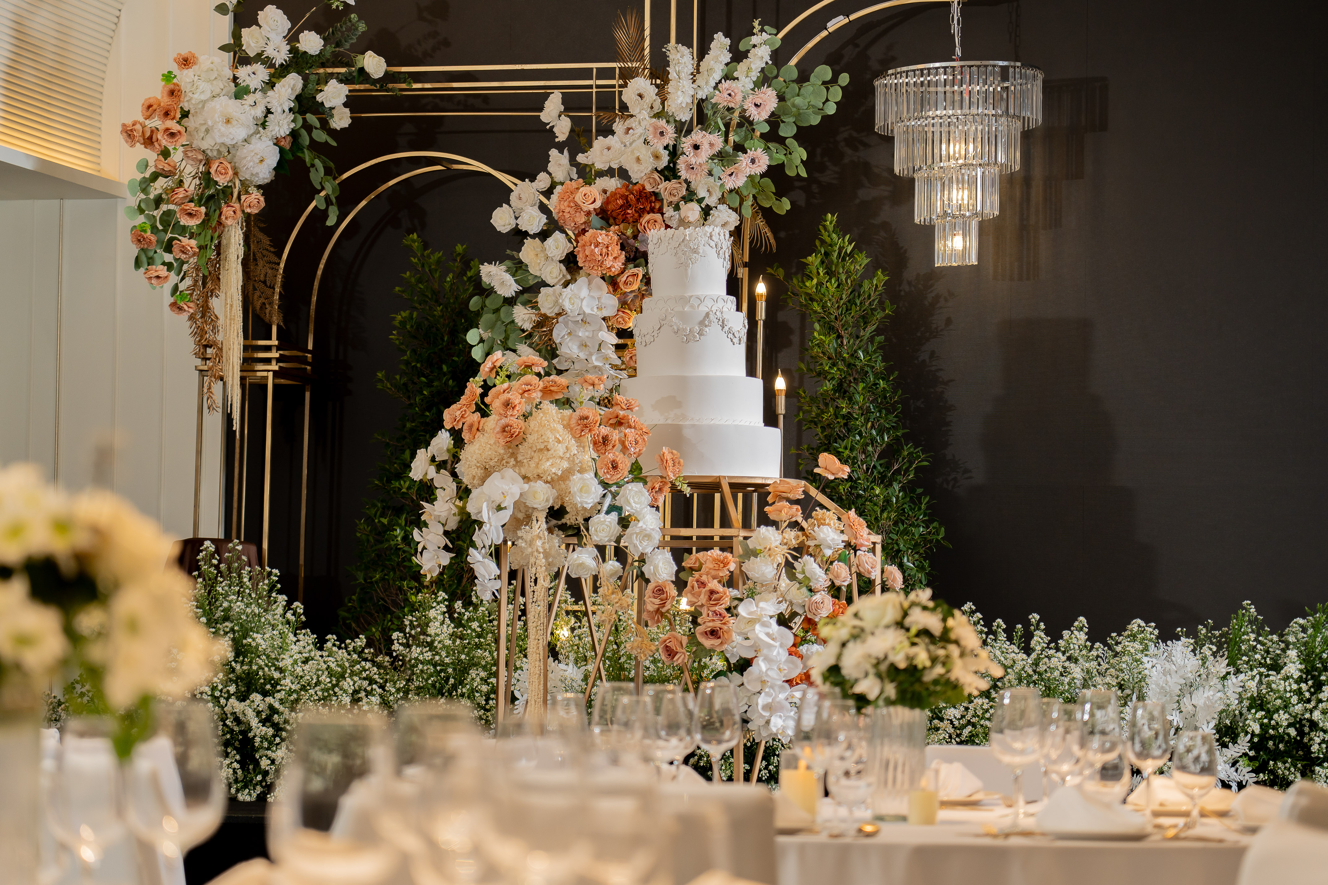 Elegant white wedding cake with peach and white floral arch, gold decor, chandelier. - Nuaan - Meliá Pattaya Hotel, Pattaya