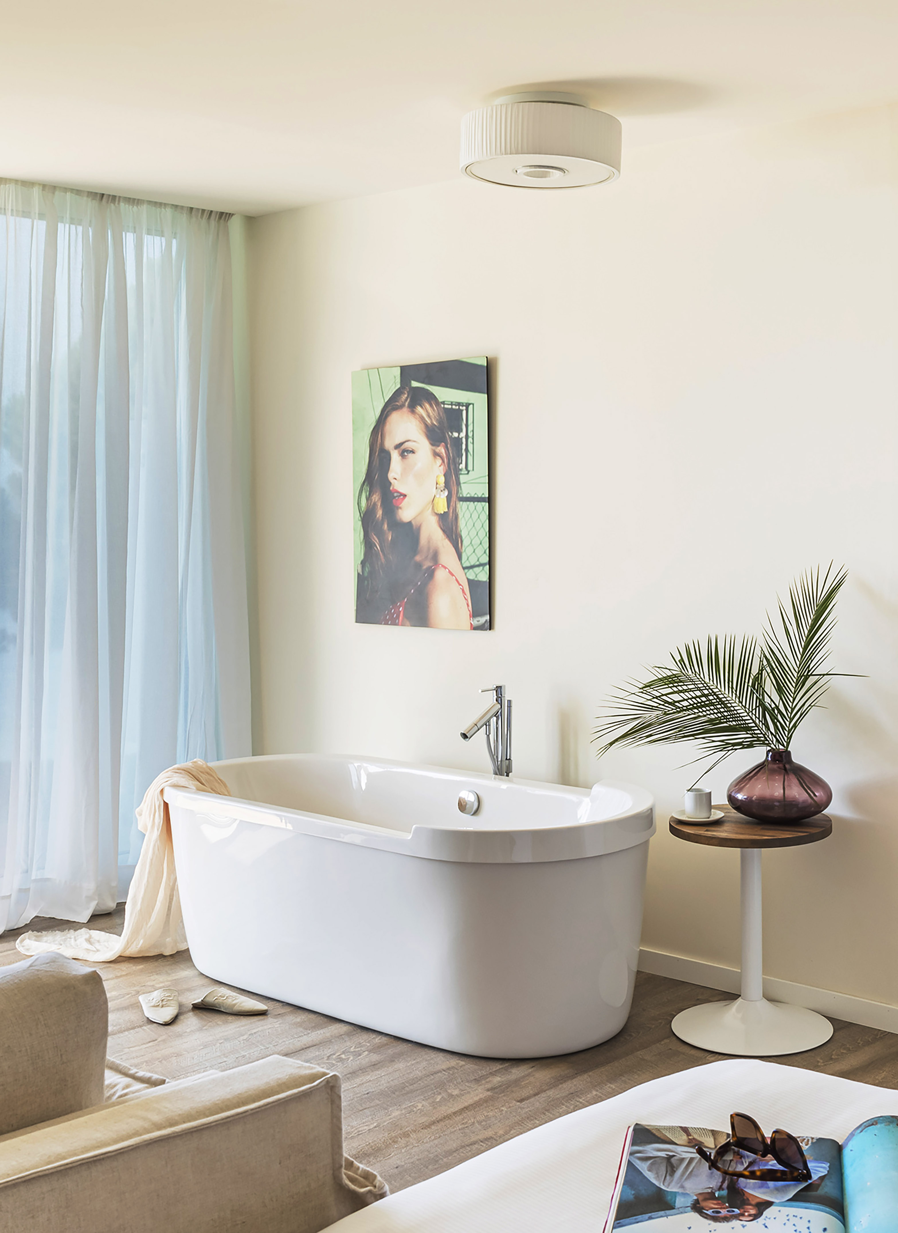 Modern bathroom with white freestanding tub, light curtains, and female portrait.