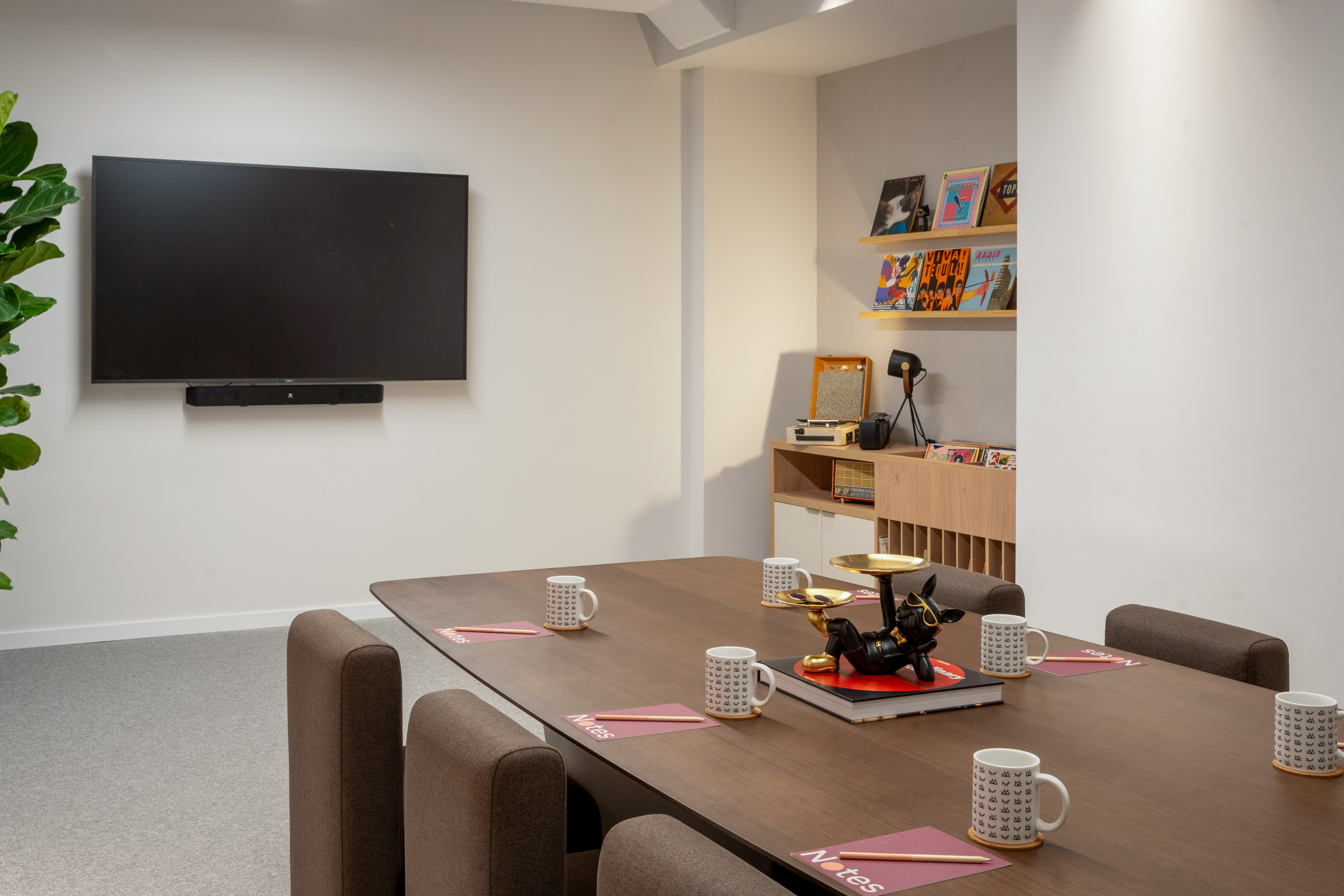 Modern meeting room with TV, wooden table, chairs, and decorative records.