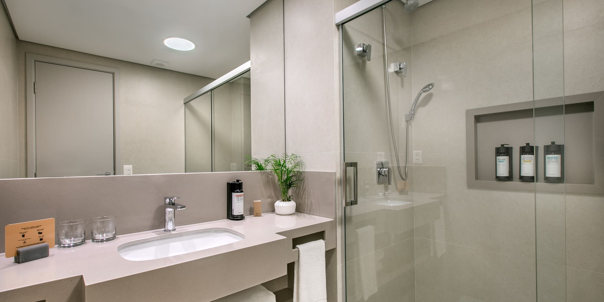 Modern hotel bathroom with vanity, sink, mirror, and glass shower.