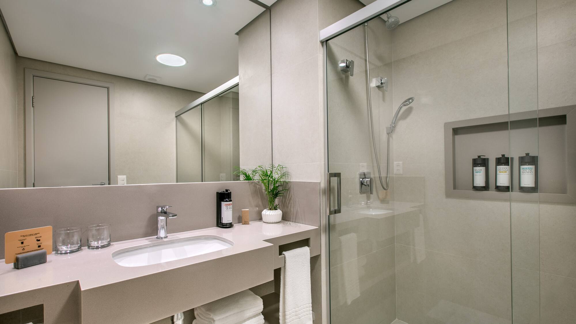 Modern hotel bathroom with vanity, sink, mirror, and glass shower.