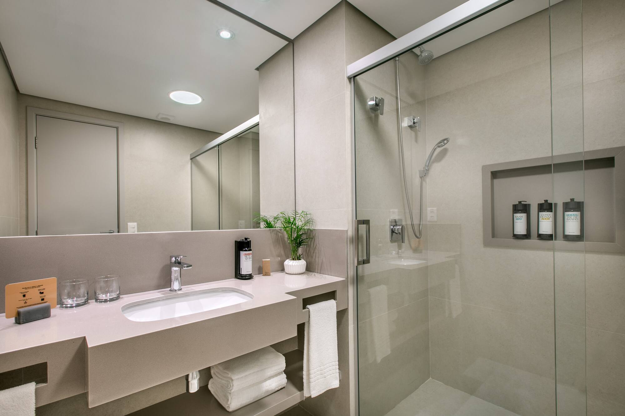 Modern hotel bathroom with vanity, sink, mirror, and glass shower.
