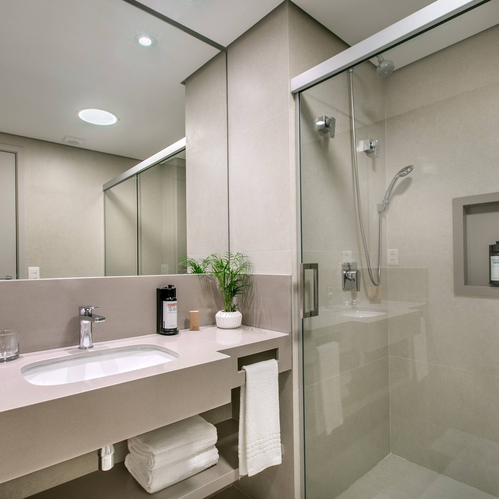 Modern hotel bathroom with vanity, sink, mirror, and glass shower.