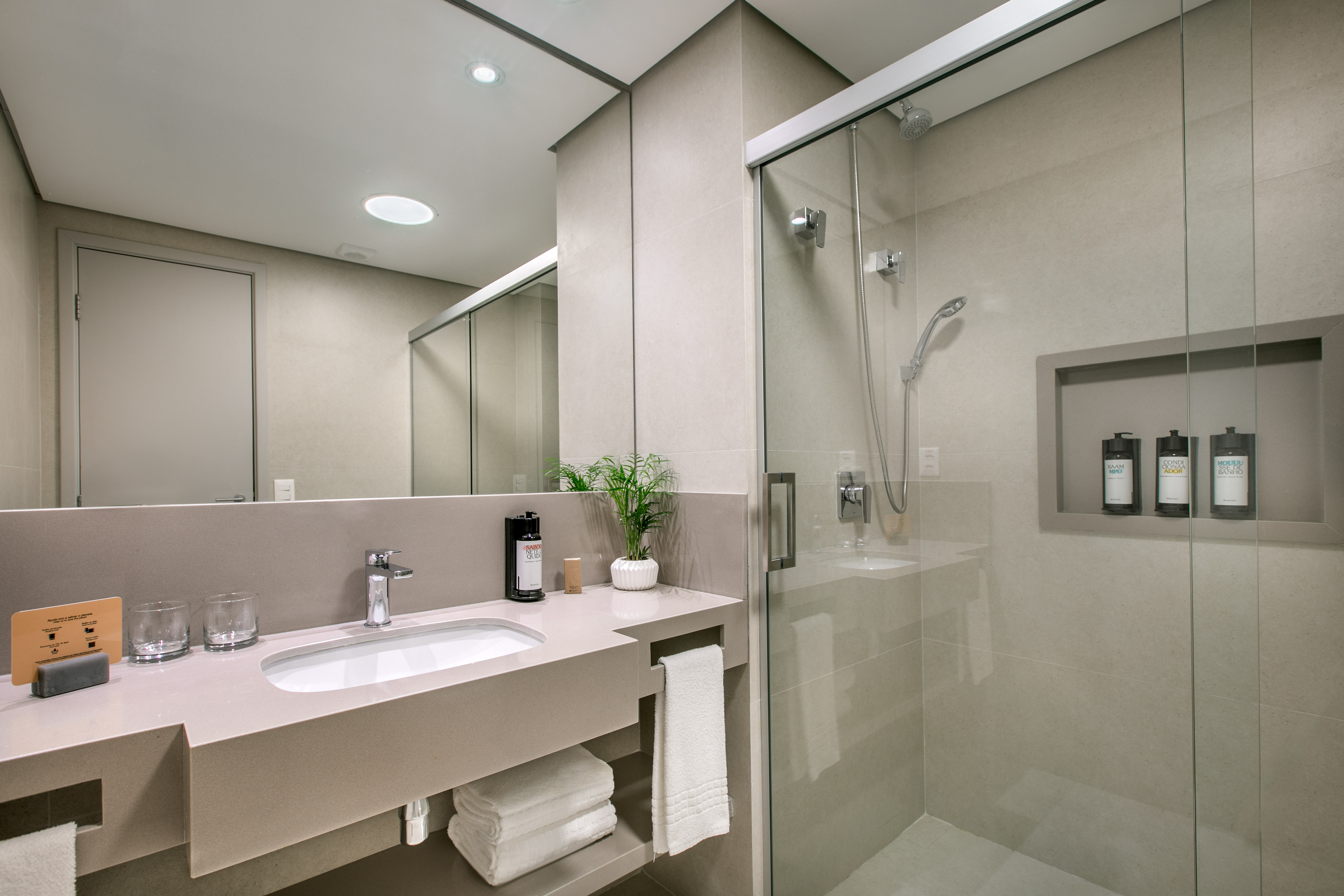 Modern hotel bathroom with vanity, sink, mirror, and glass shower.