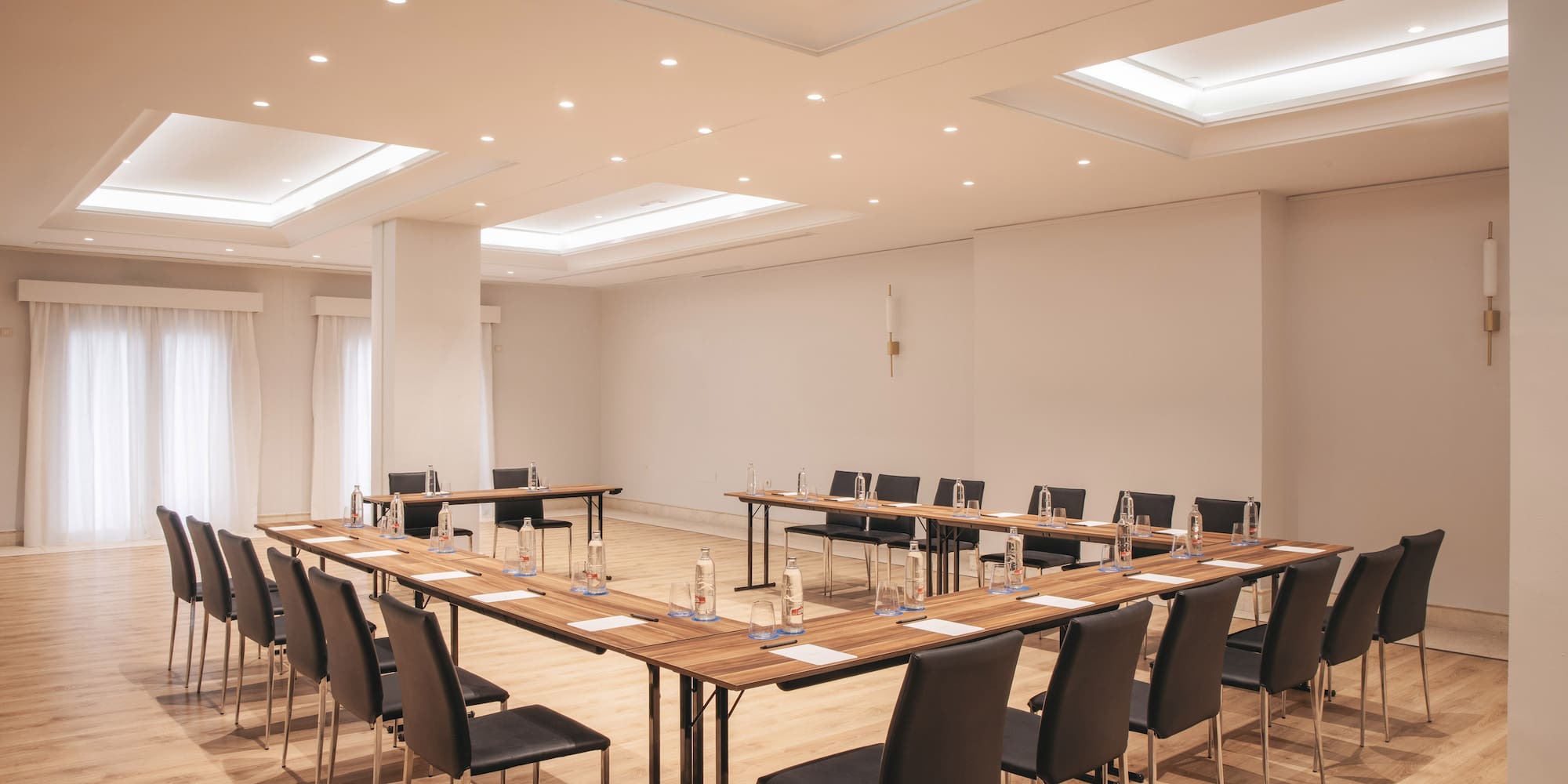 Modern hotel conference room with U-shaped table setup and bright lighting.