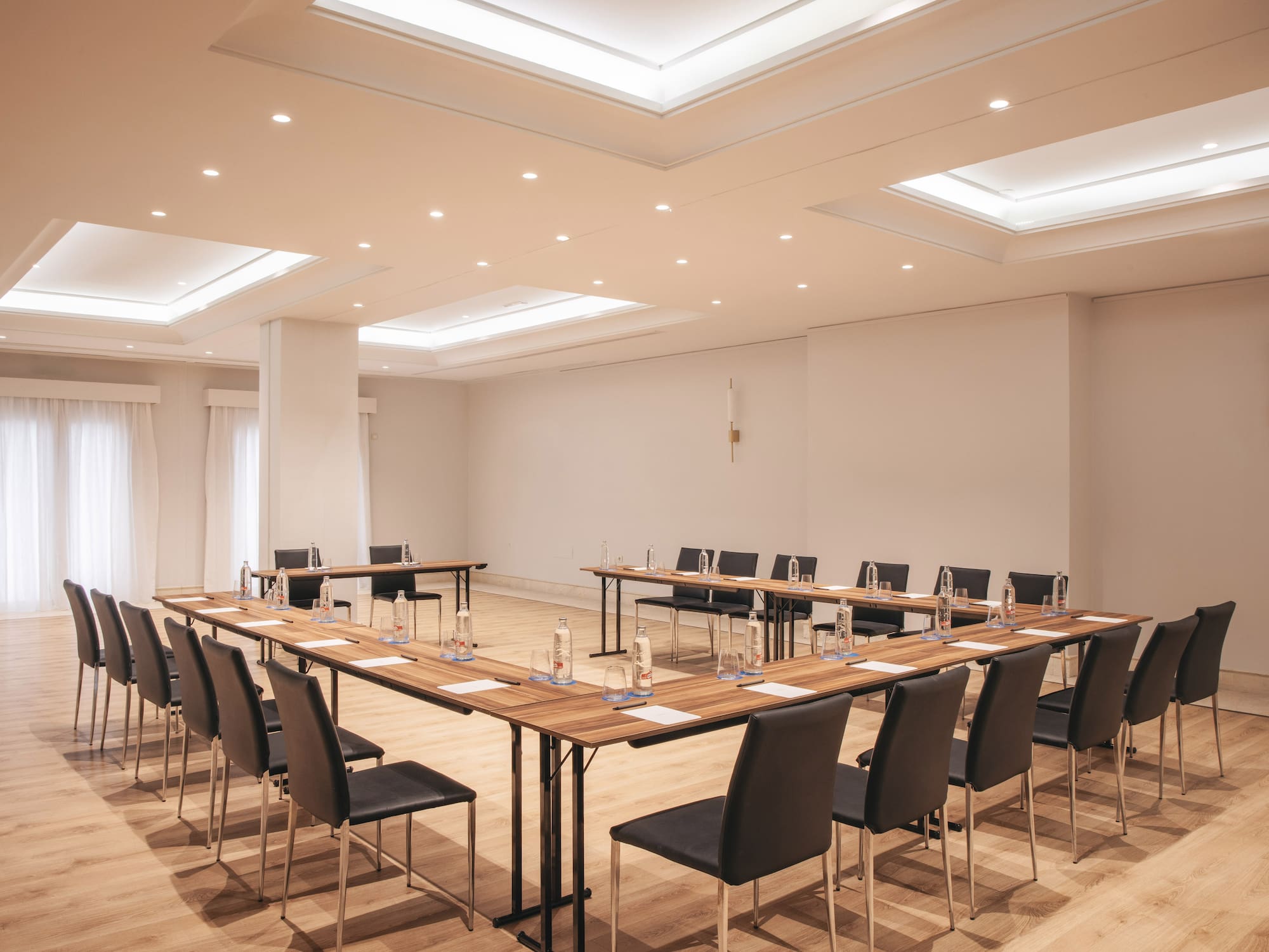 Bright U-shaped conference room with modern tables, black chairs, and wood floor.