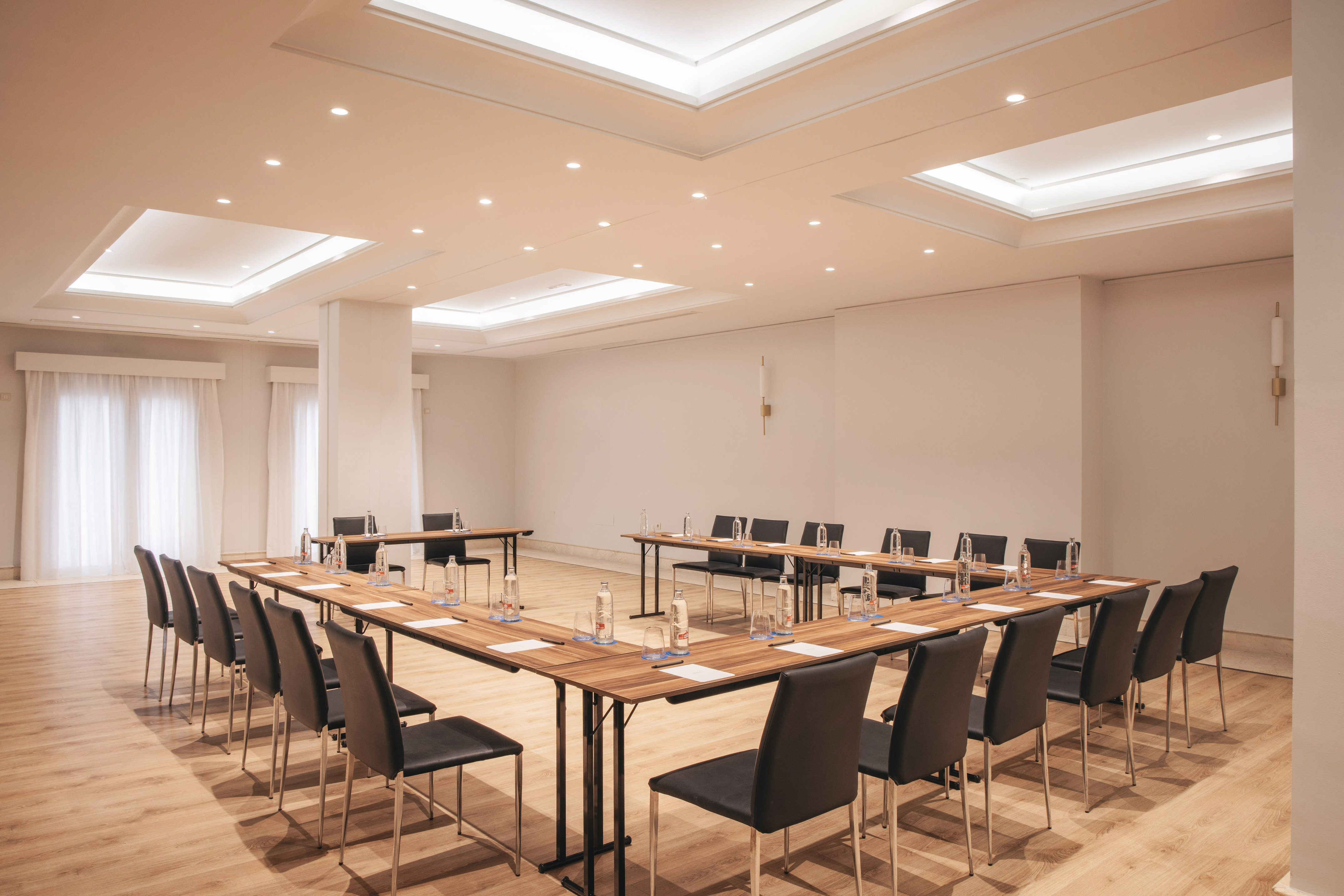 Bright U-shaped conference room with modern tables, black chairs, and wood floor.