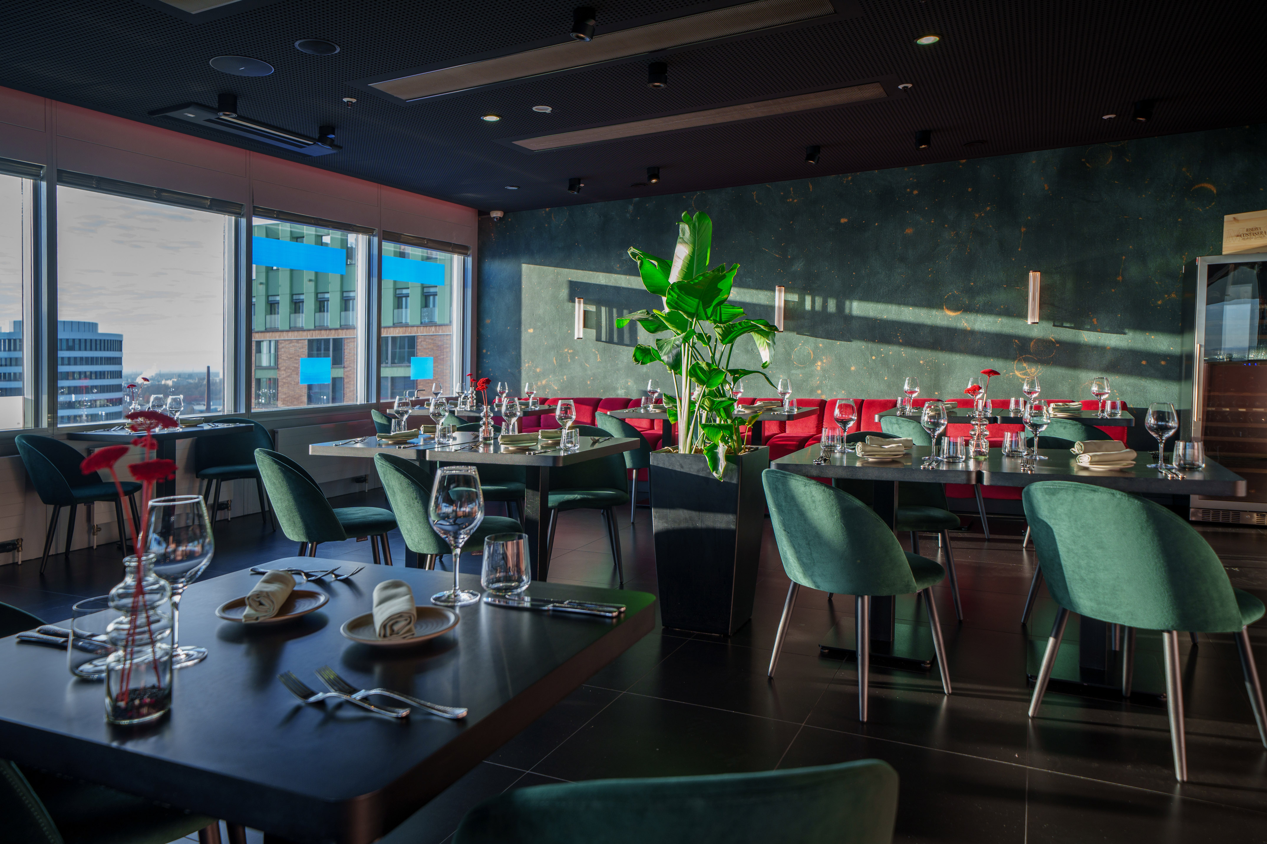 Modern dining room with city view, green velvet chairs, and red banquettes.