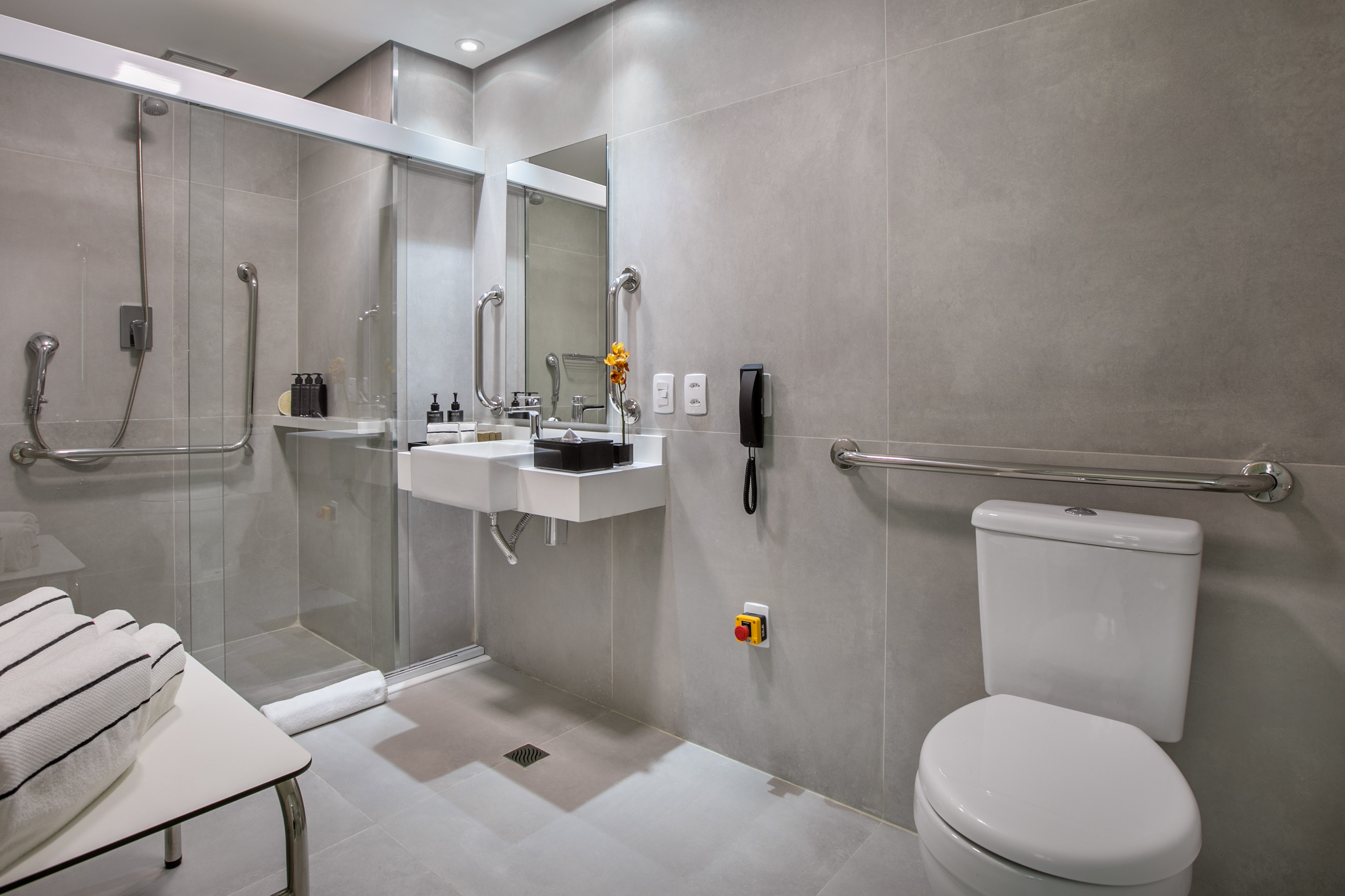 Accessible grey tiled bathroom with roll-in shower, grab bars, and emergency button.