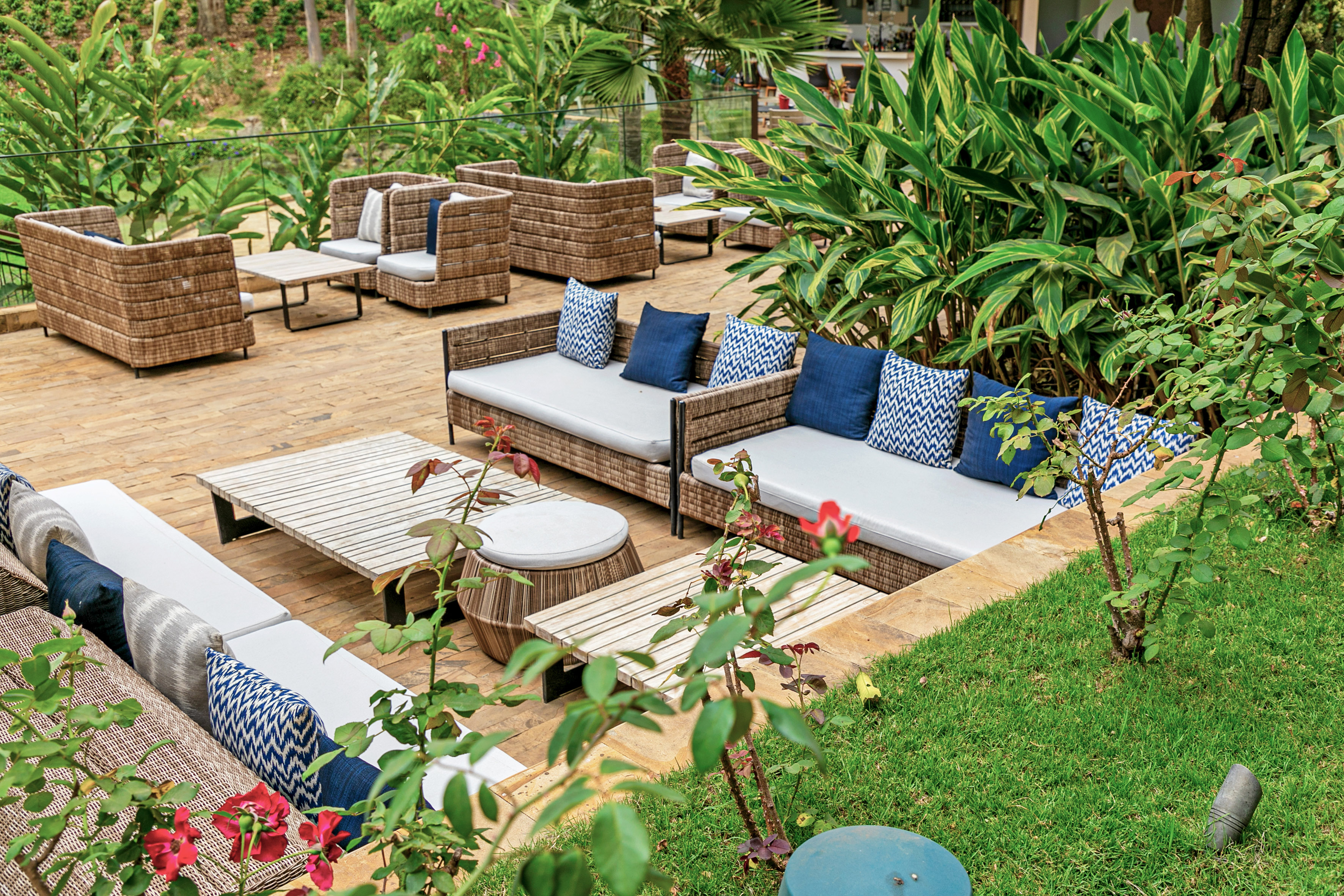 Outdoor patio lounge with wicker sofas, blue pillows, and lush tropical plants.