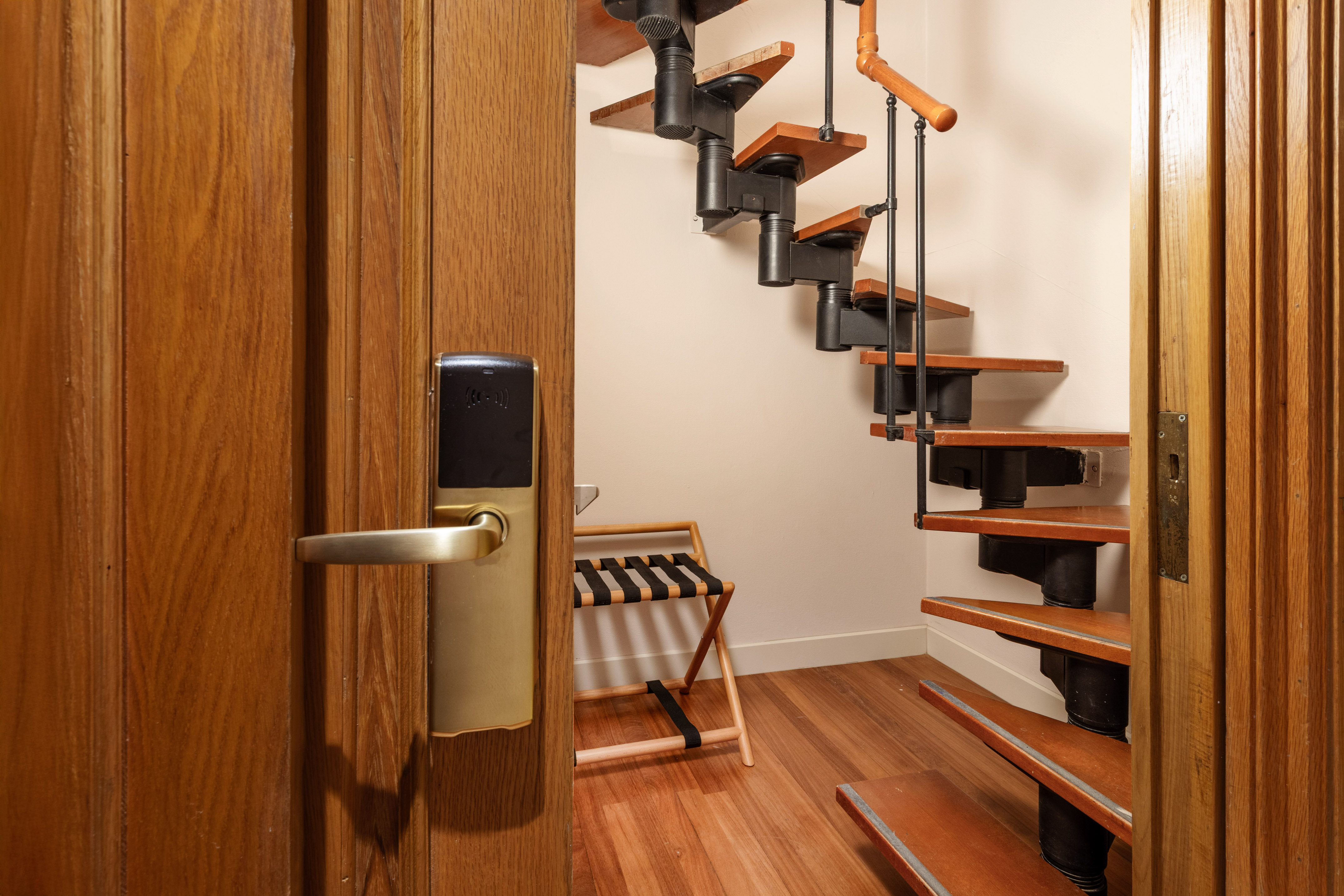 Hotel room entrance with smart lock, wooden spiral staircase, and luggage rack.