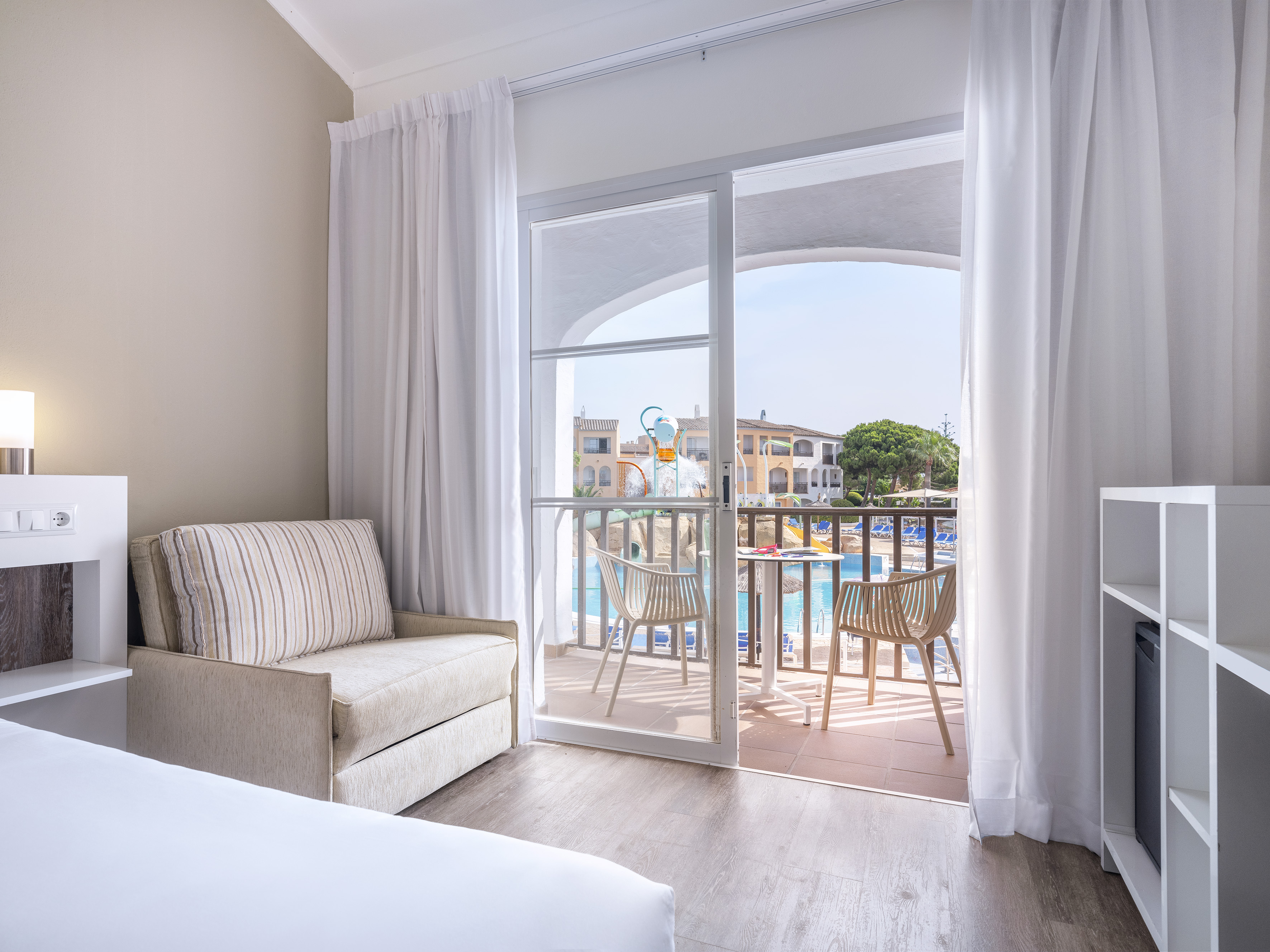 Hotel room with balcony overlooking a swimming pool and water park.