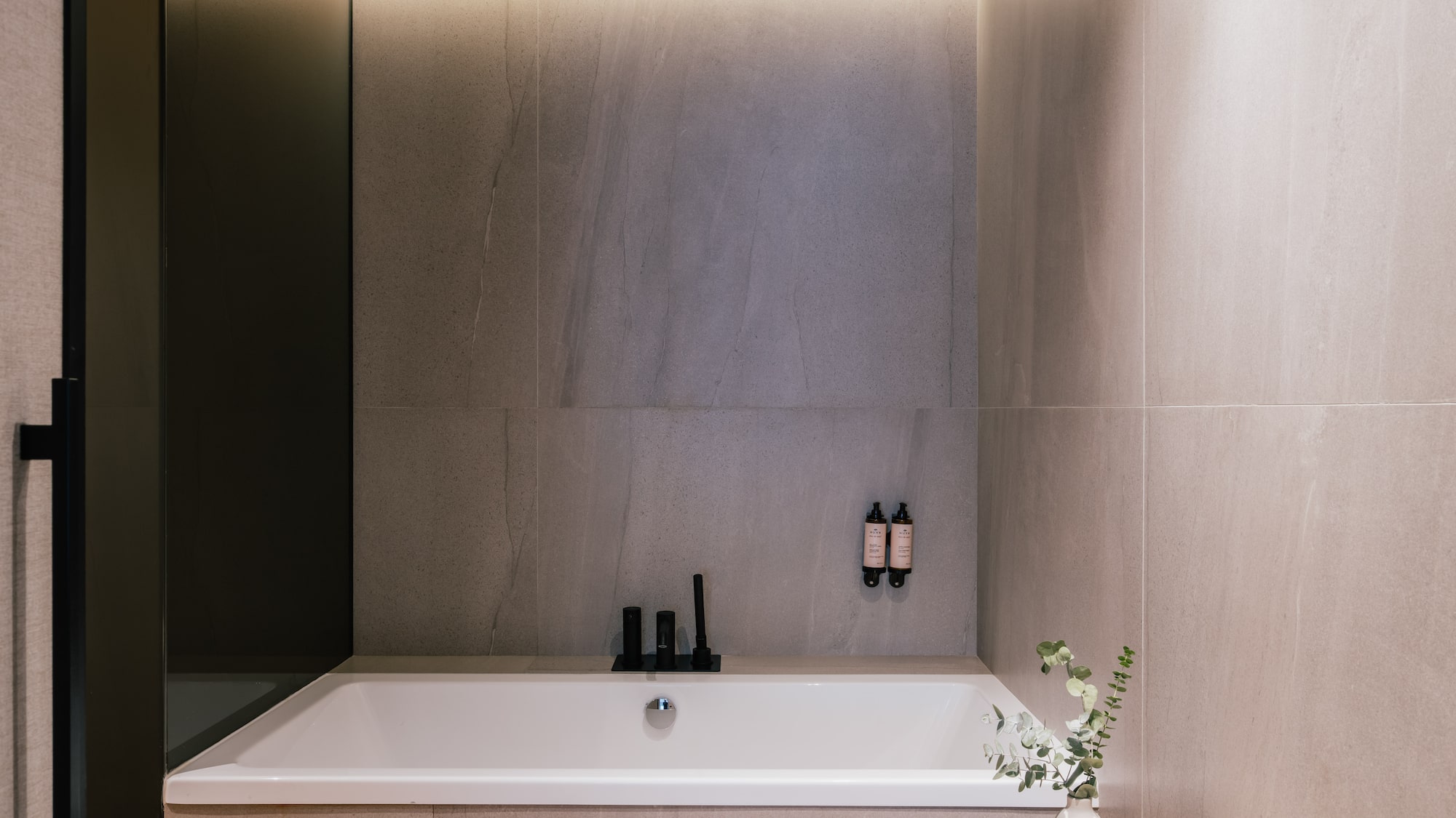 Modern bathroom with white tub, grey tiles, black fixtures, and LED lighting.