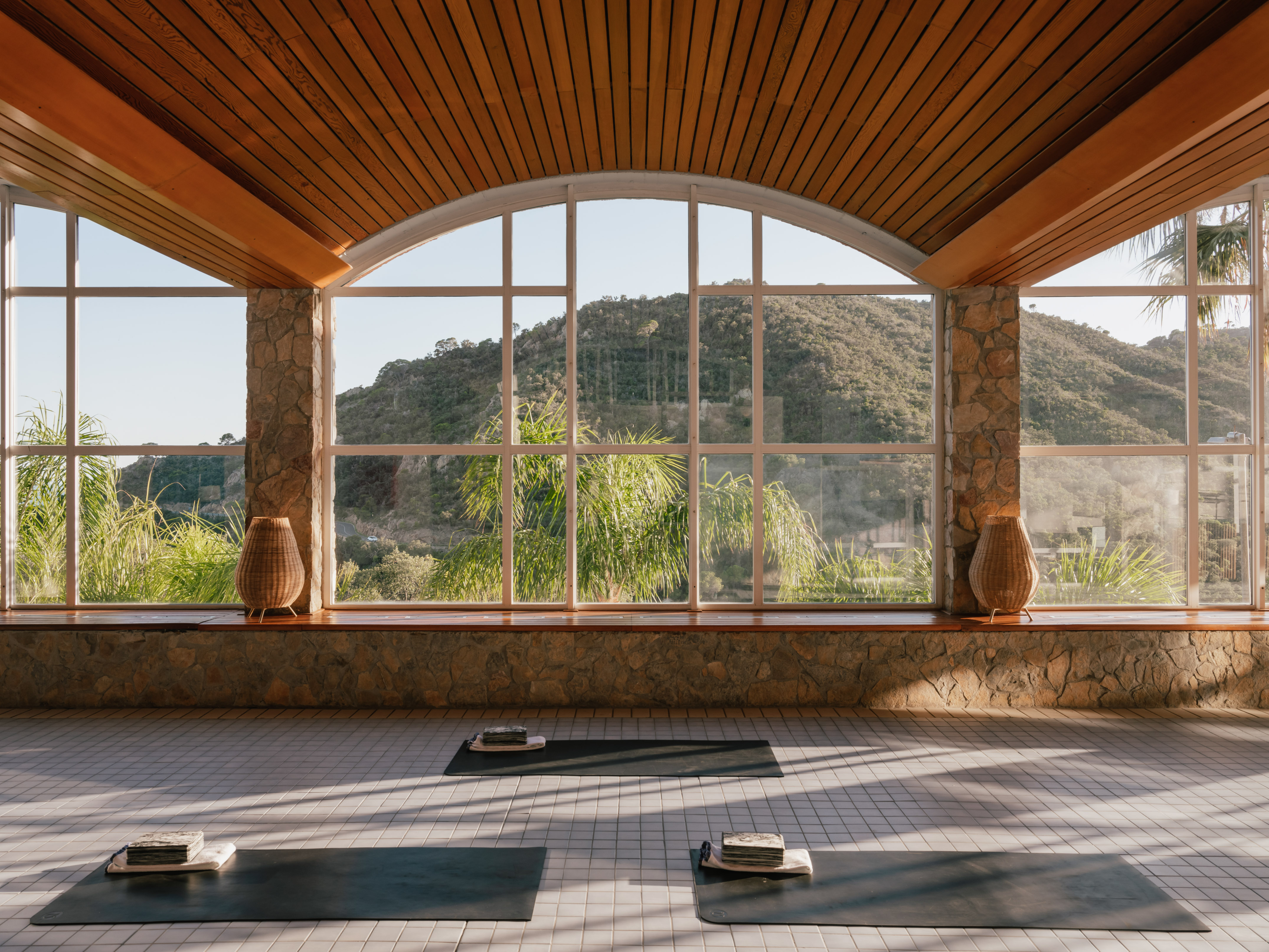 Serene wellness yoga studio with mountain view, arched windows, and wood ceiling.