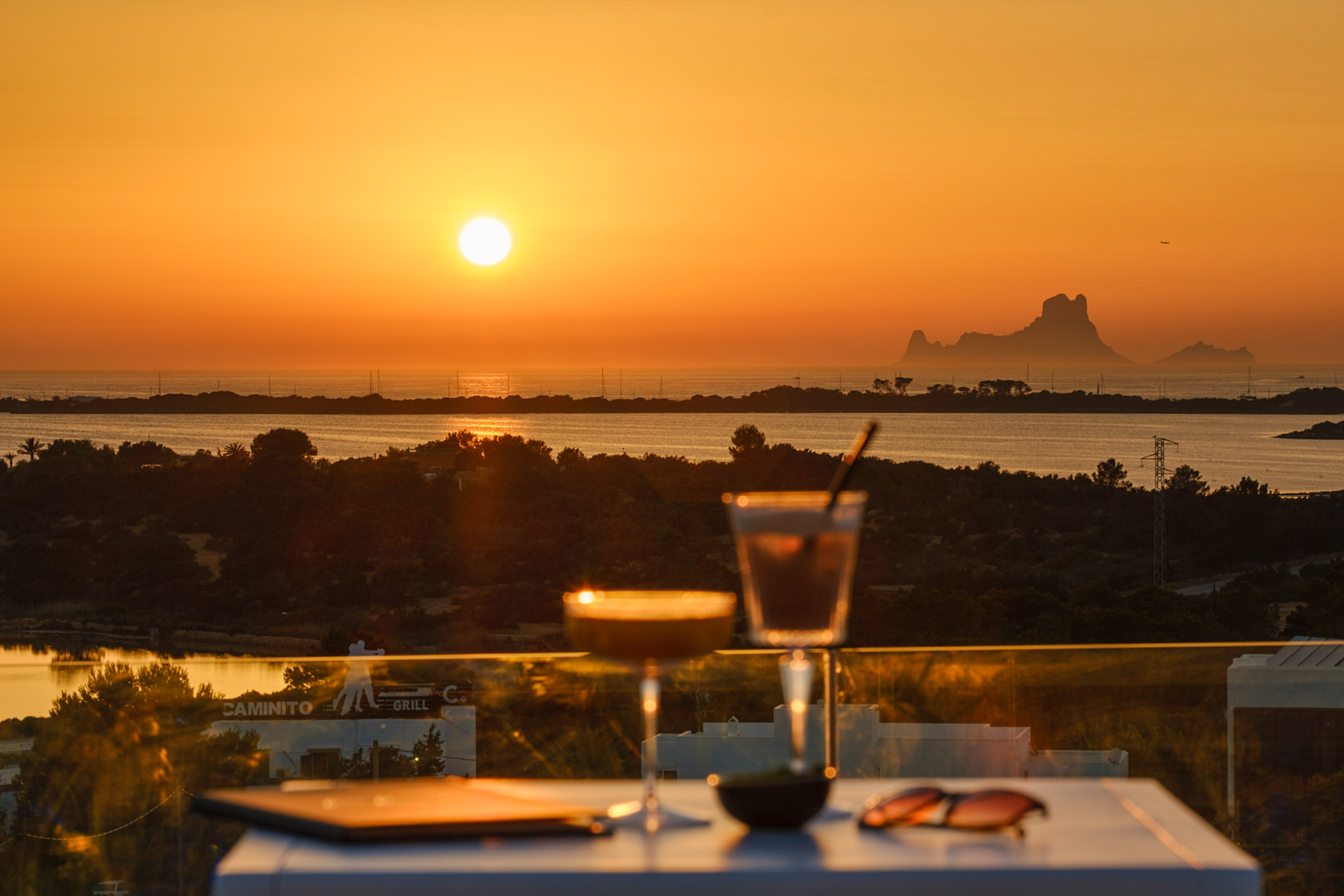 Sunset cocktails on a terrace with ocean view and distant Es Vedrà island.