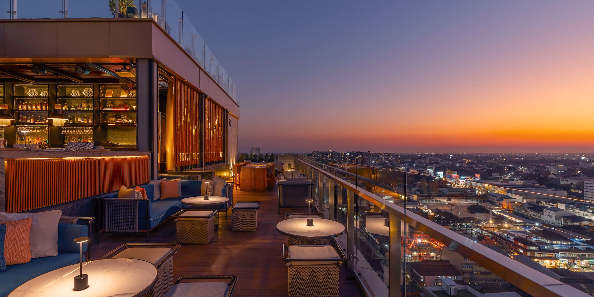 a rooftop bar with tables and chairs and a city skyline
