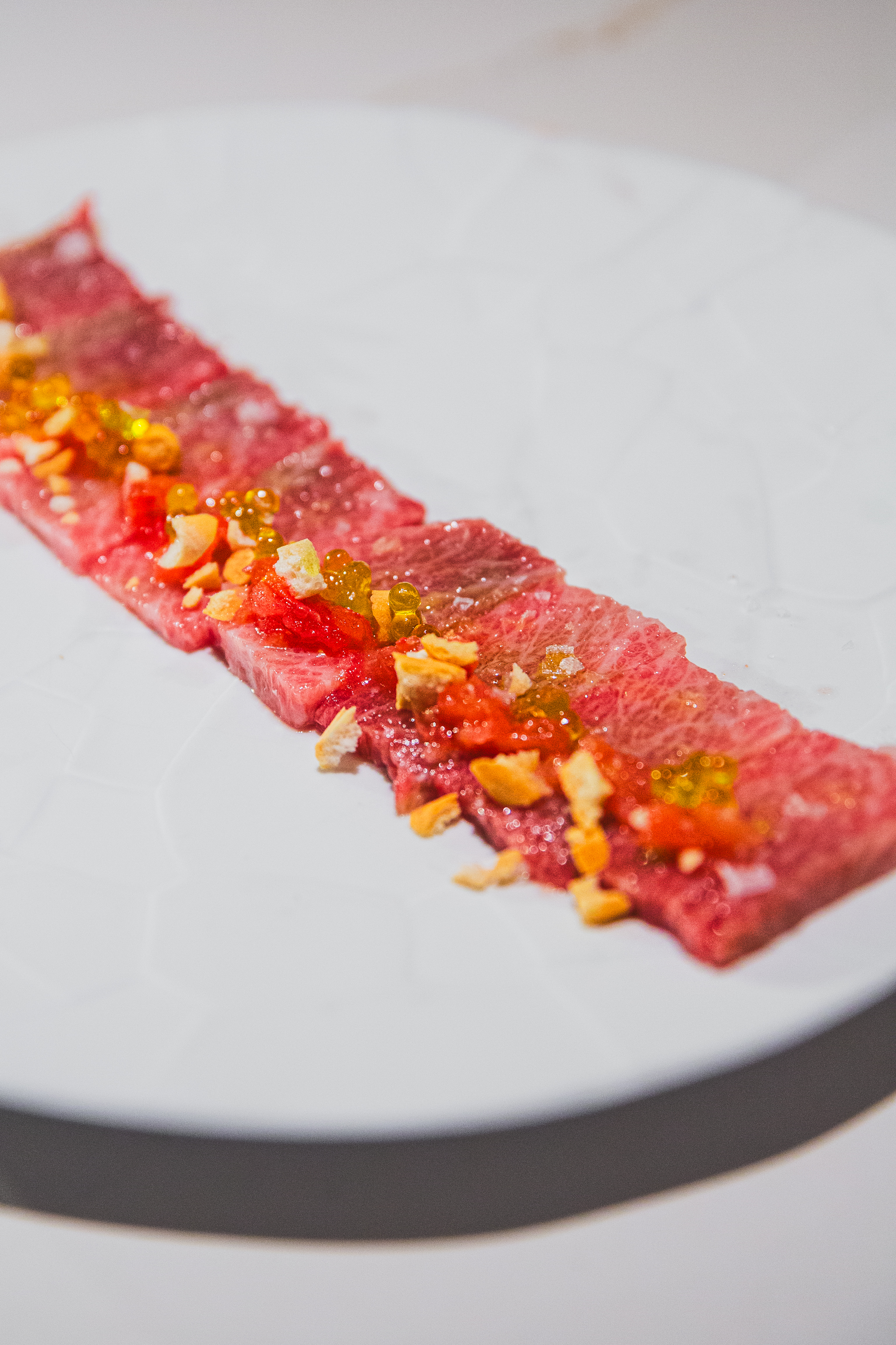 Wagyu beef carpaccio with garlic, tomato, and golden caviar pearls on white.