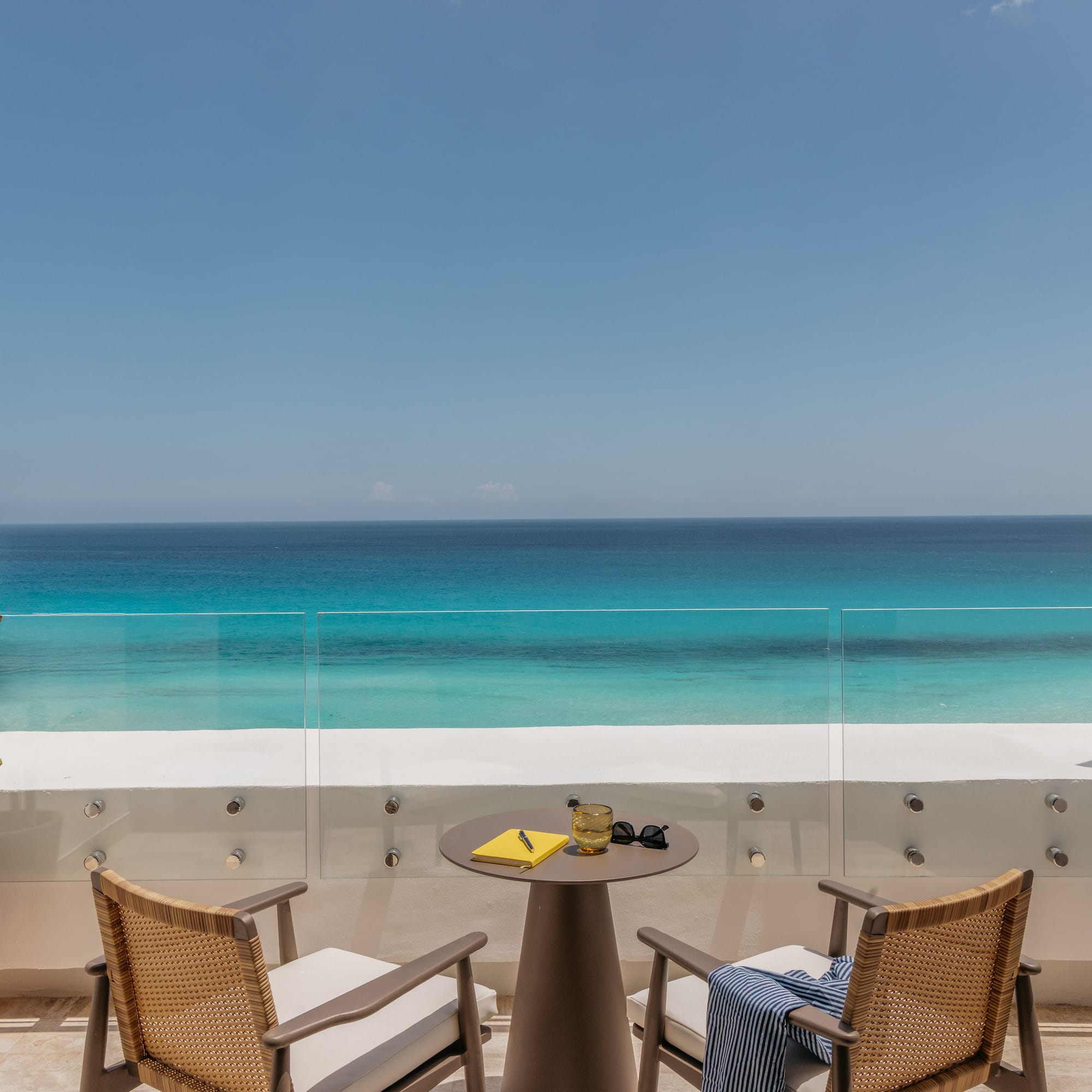 Hotel balcony with chairs, table, and stunning turquoise ocean view.