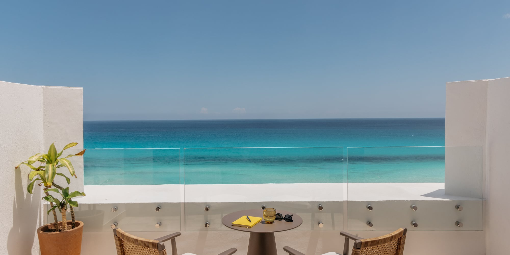 Hotel balcony with chairs, table, and stunning turquoise ocean view.
