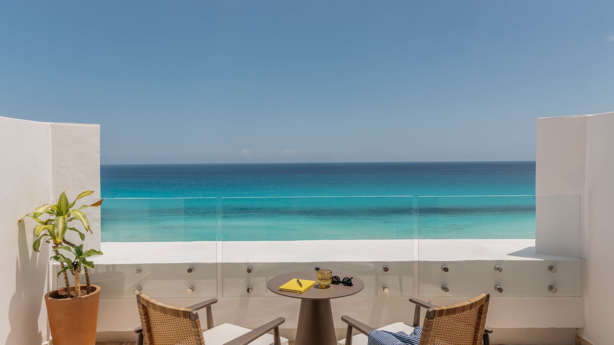 Hotel balcony with chairs, table, and stunning turquoise ocean view.