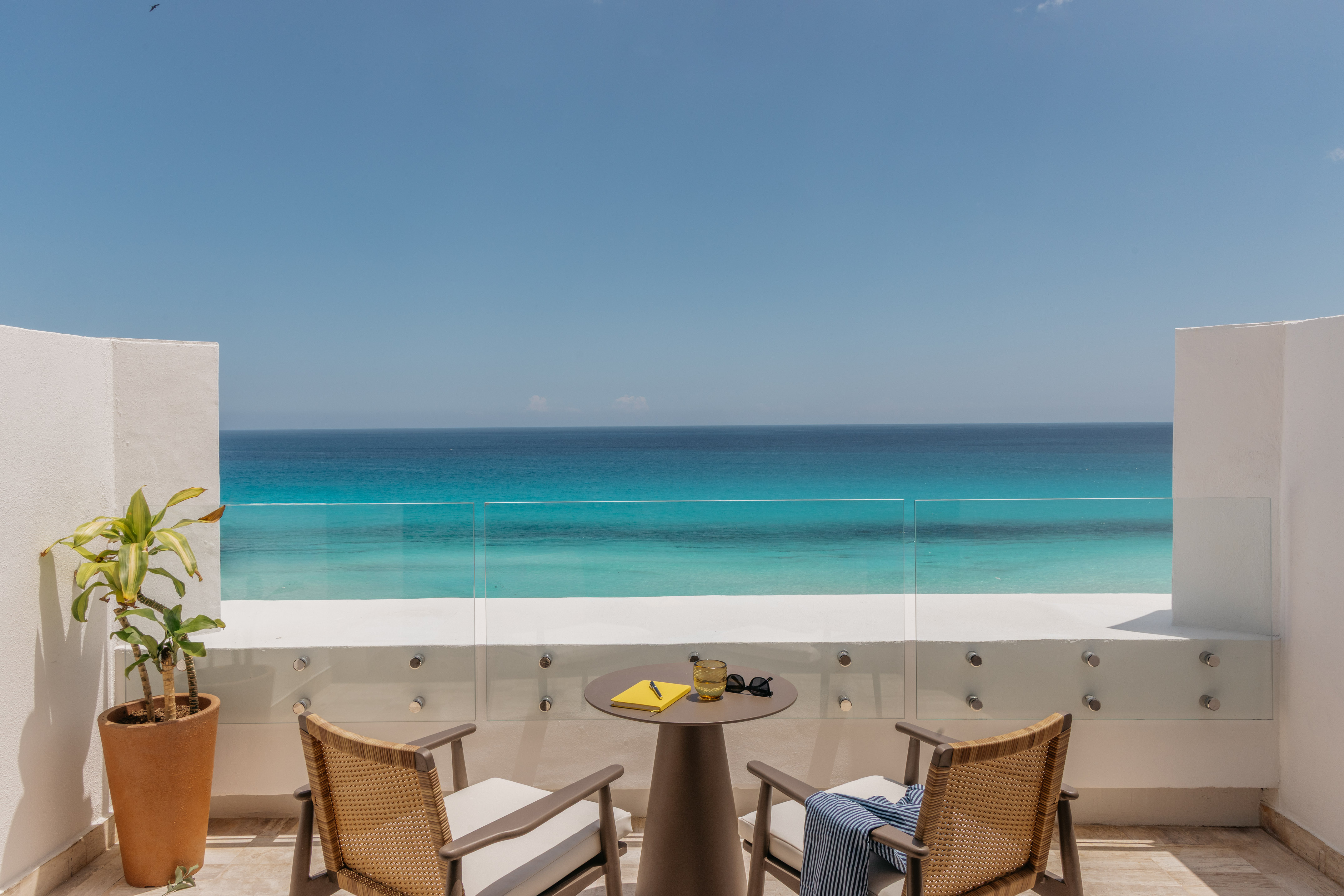 Hotel balcony with chairs, table, and stunning turquoise ocean view.