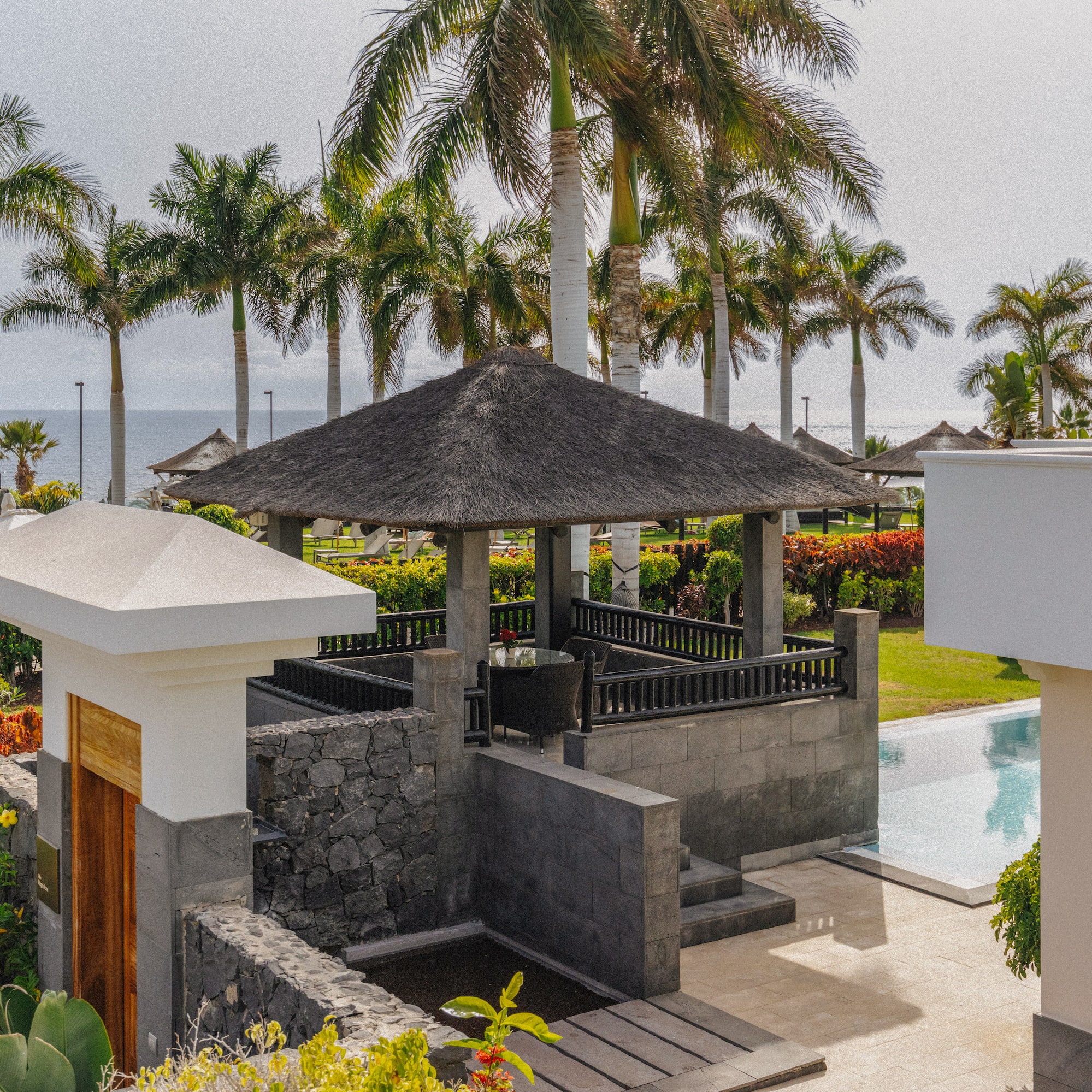 Tropical resort with palm trees, thatched gazebo, pool, and ocean view.