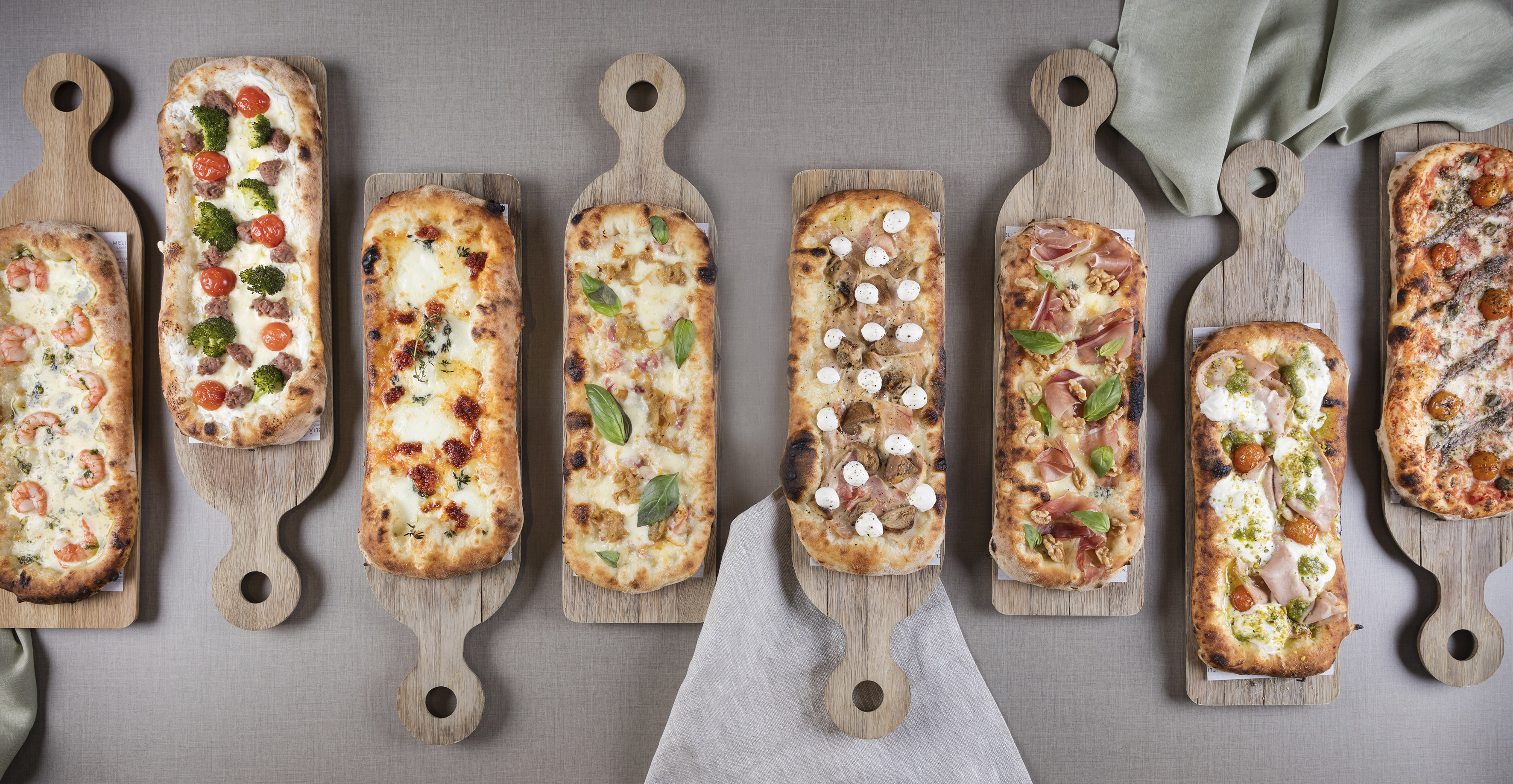 Seven rectangular Pinsa Romana pizzas on wooden boards with varied toppings.