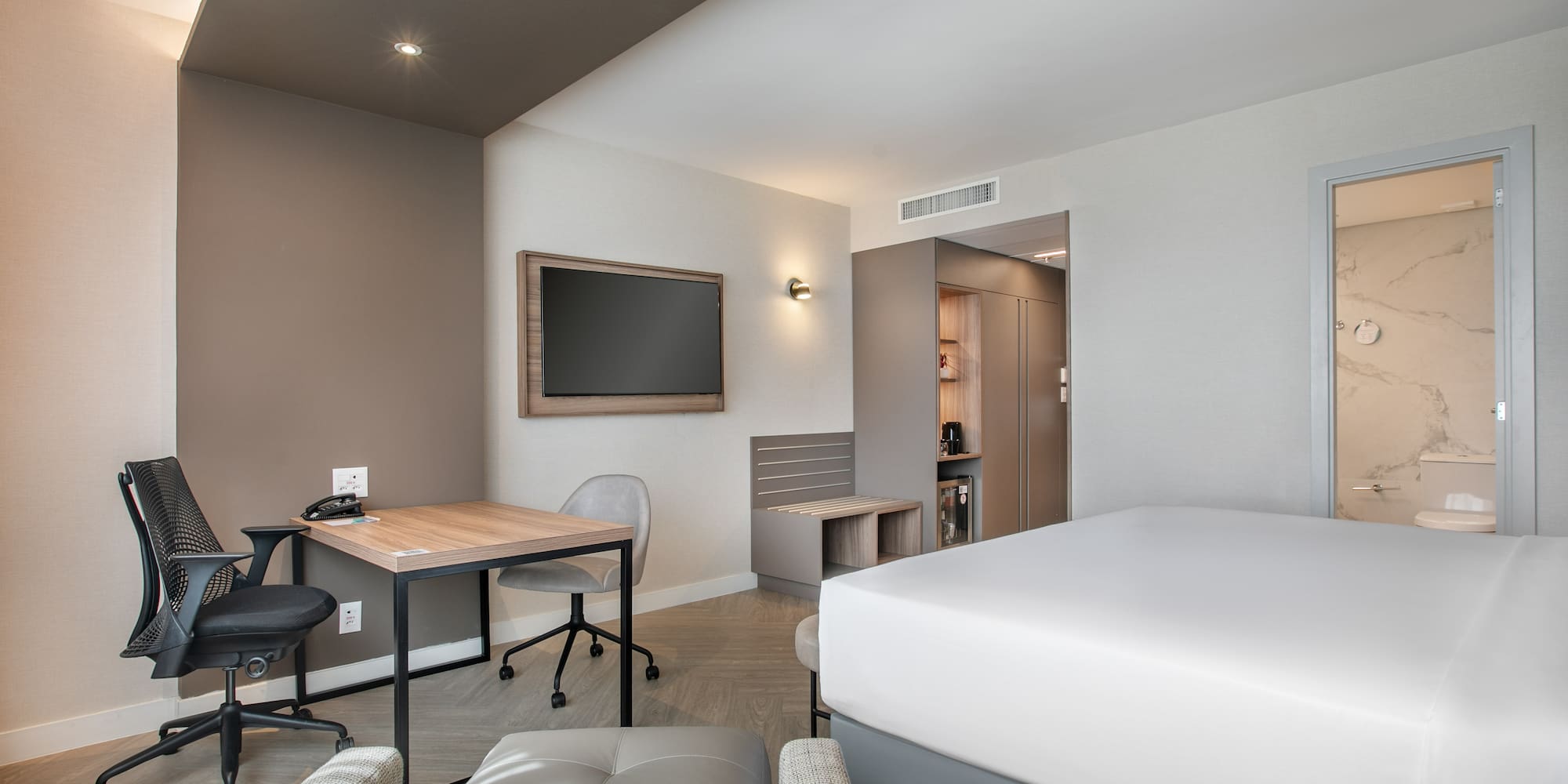 Sleek hotel room with bed, work desk, wall-mounted TV, and private bathroom.