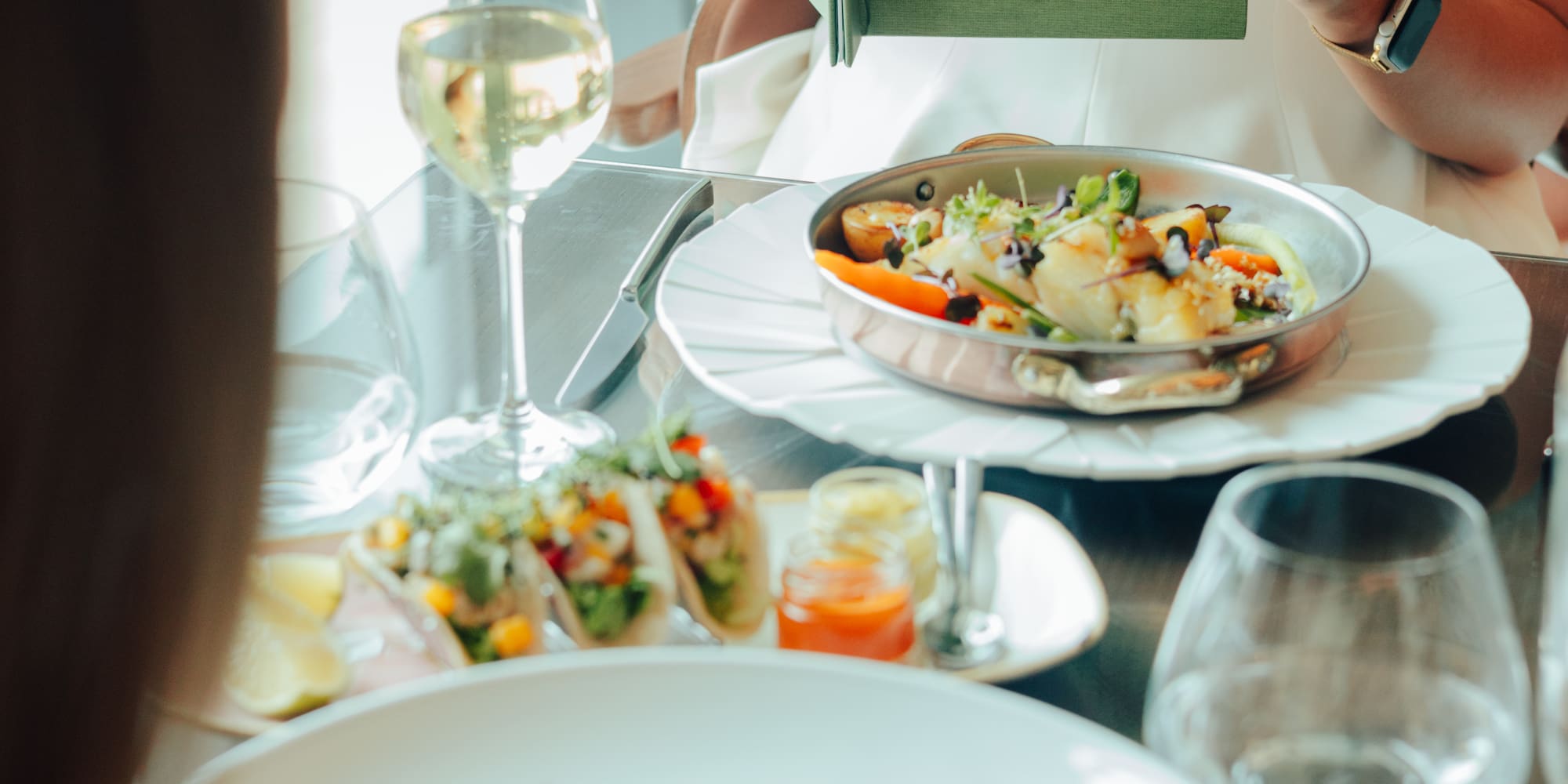 Woman holds 'Colinas de Lisboa' menu; seafood and wine on restaurant table.