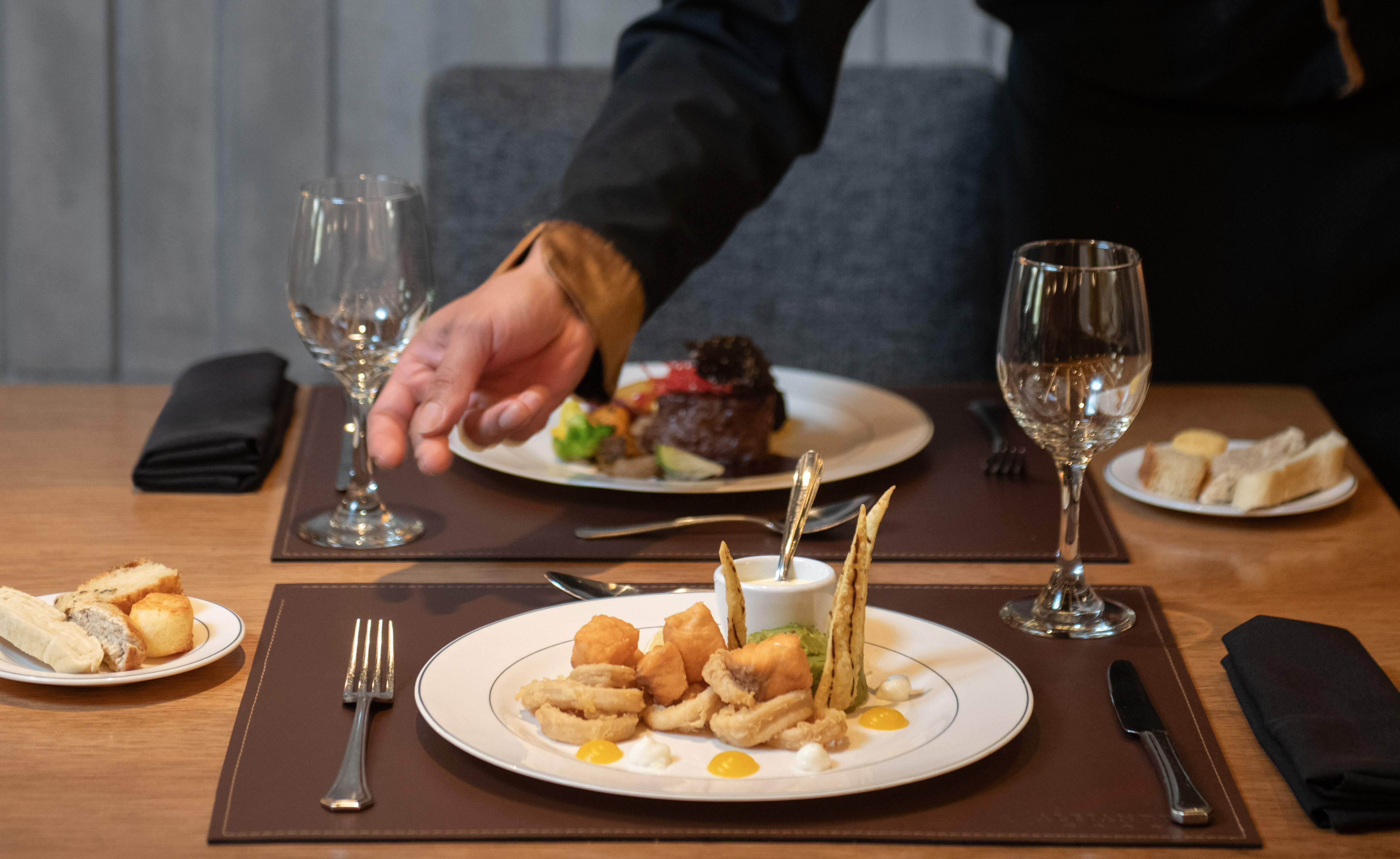 Waiter serving fried seafood and steak at an upscale restaurant table.
