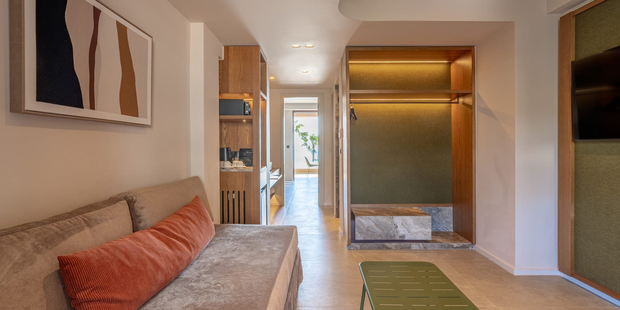 Contemporary hotel suite featuring living area, kitchenette, and open wardrobe.