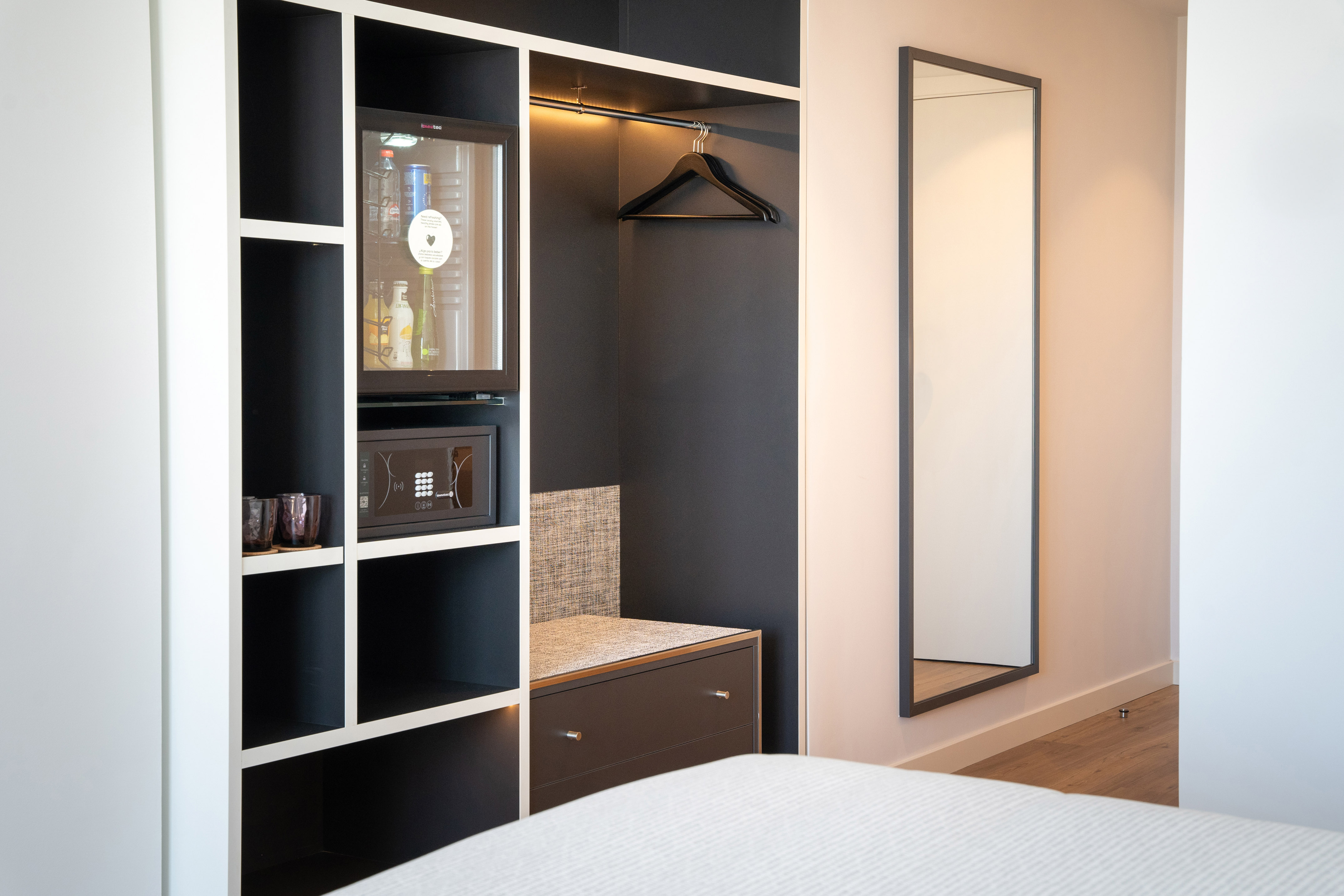 Sleek hotel room built-in wardrobe with minibar, safe, hangers, and mirror.