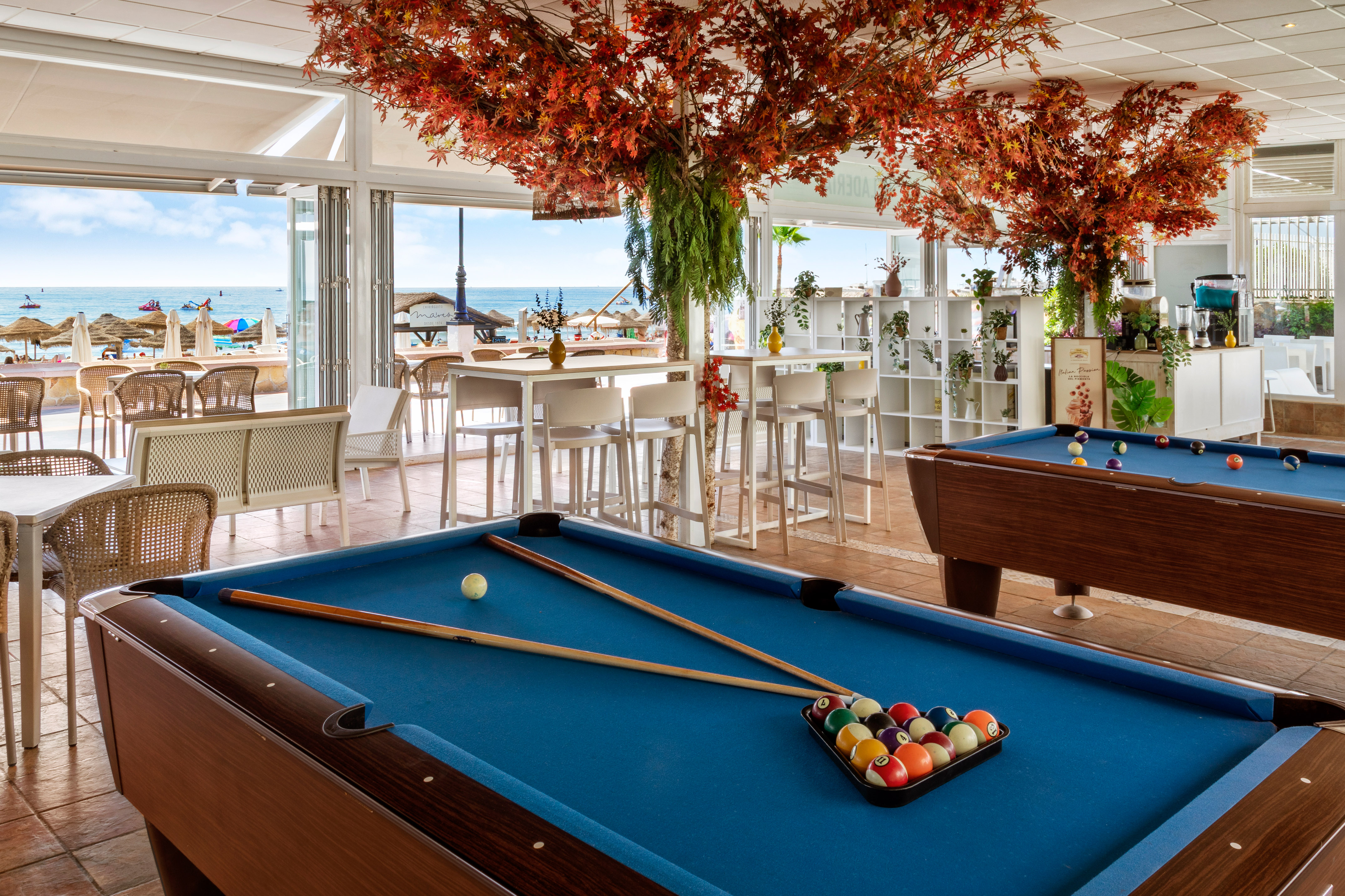 Coastal lounge with billiards tables, red foliage, and ocean view.