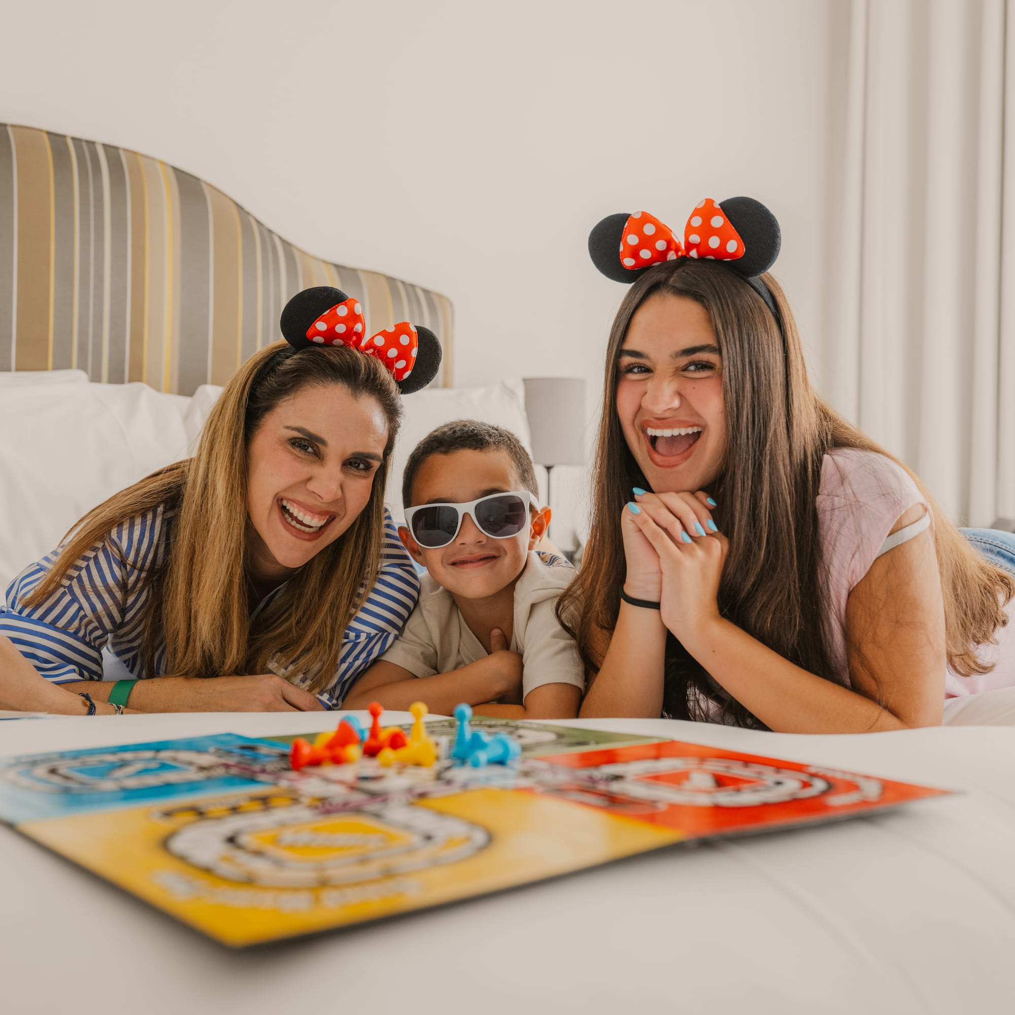 Smiling family with Minnie Mouse ears playing board game on hotel bed. - Meliá Orlando Celebration, Orlando