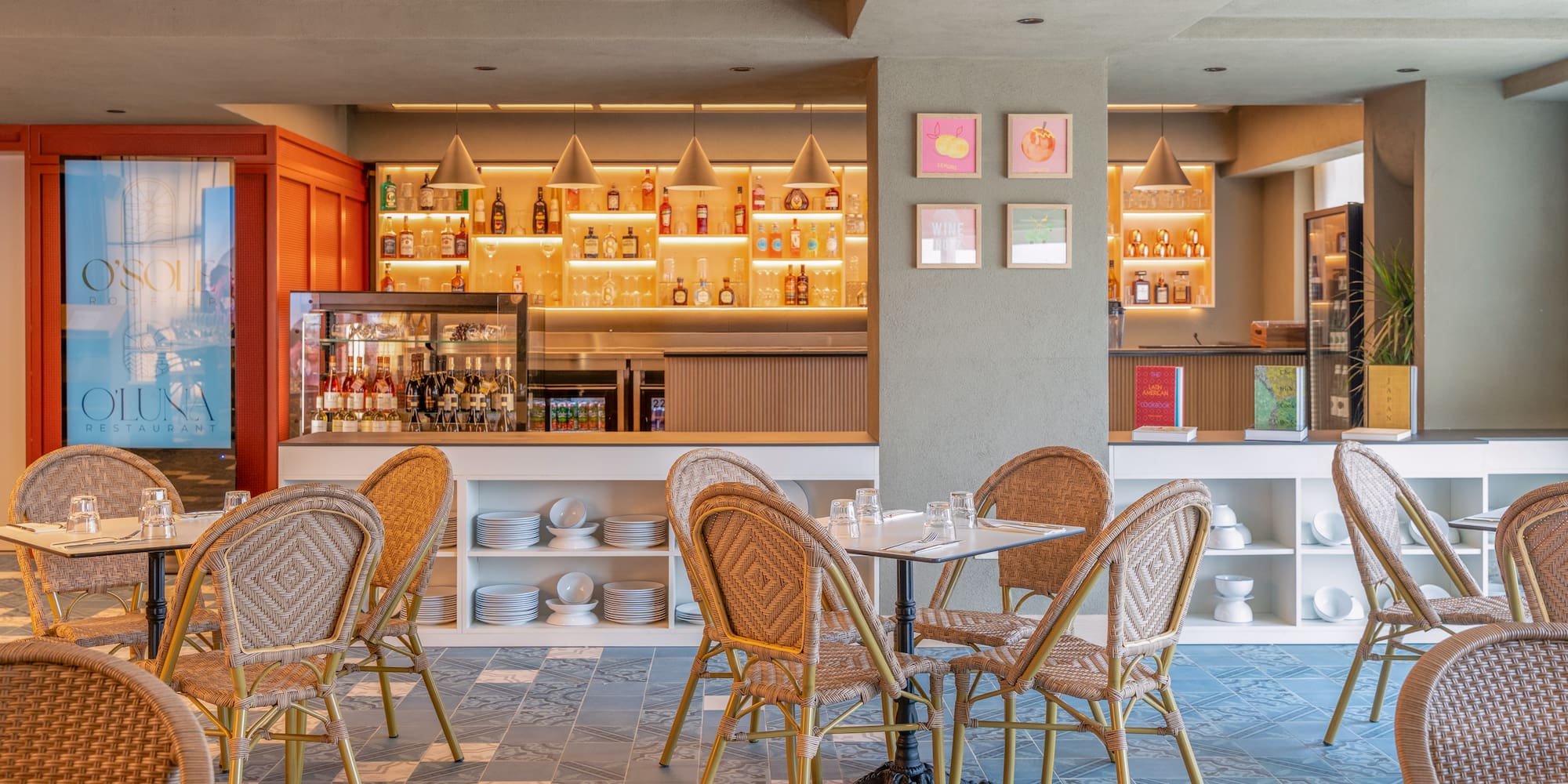Restaurant dining room with illuminated bar, wicker chairs, and blue patterned floor.